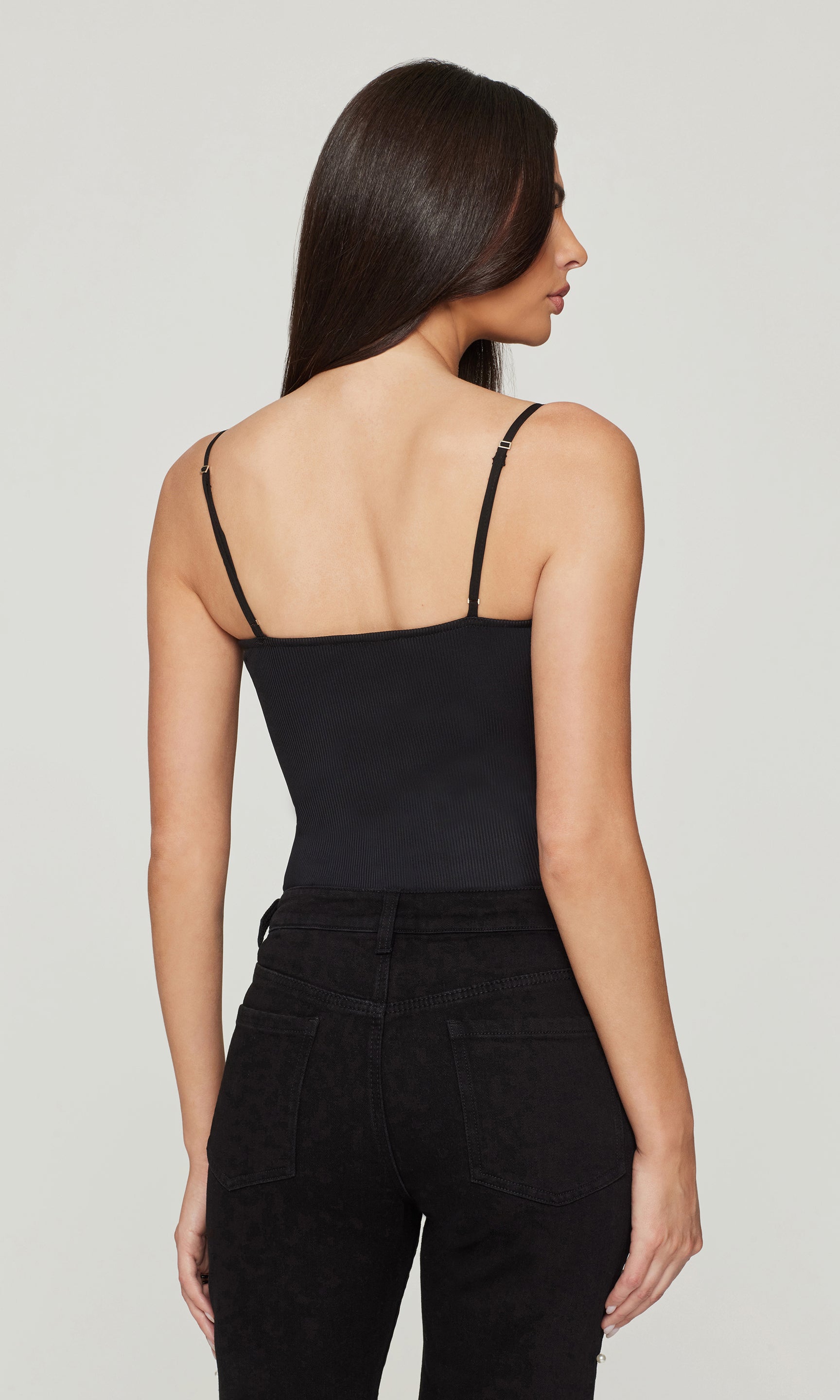Back view image of model wearing a black cami and black pants on a white background