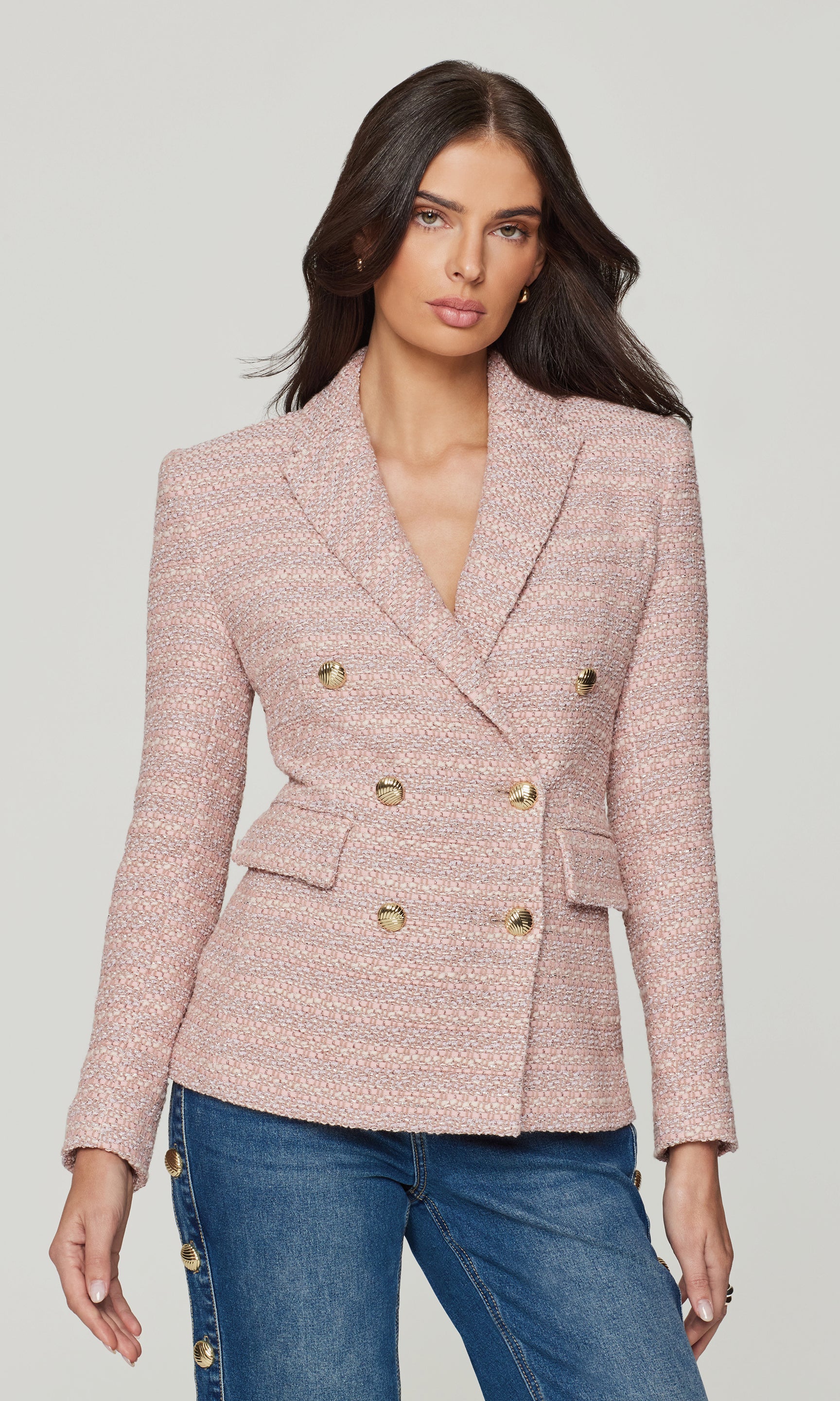 Woman wearing a pink tweed blazer with gold buttons on a gray background