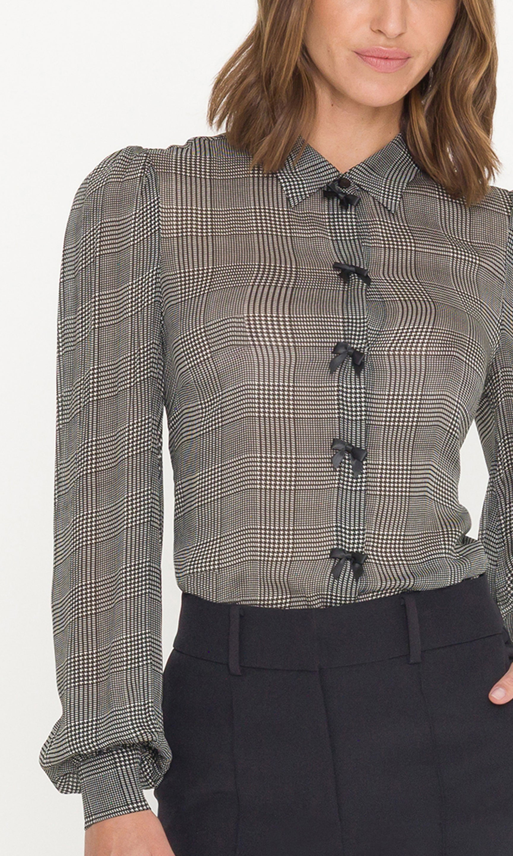 Woman wearing a gray checkered blouse with black bows and black pants on a white background
