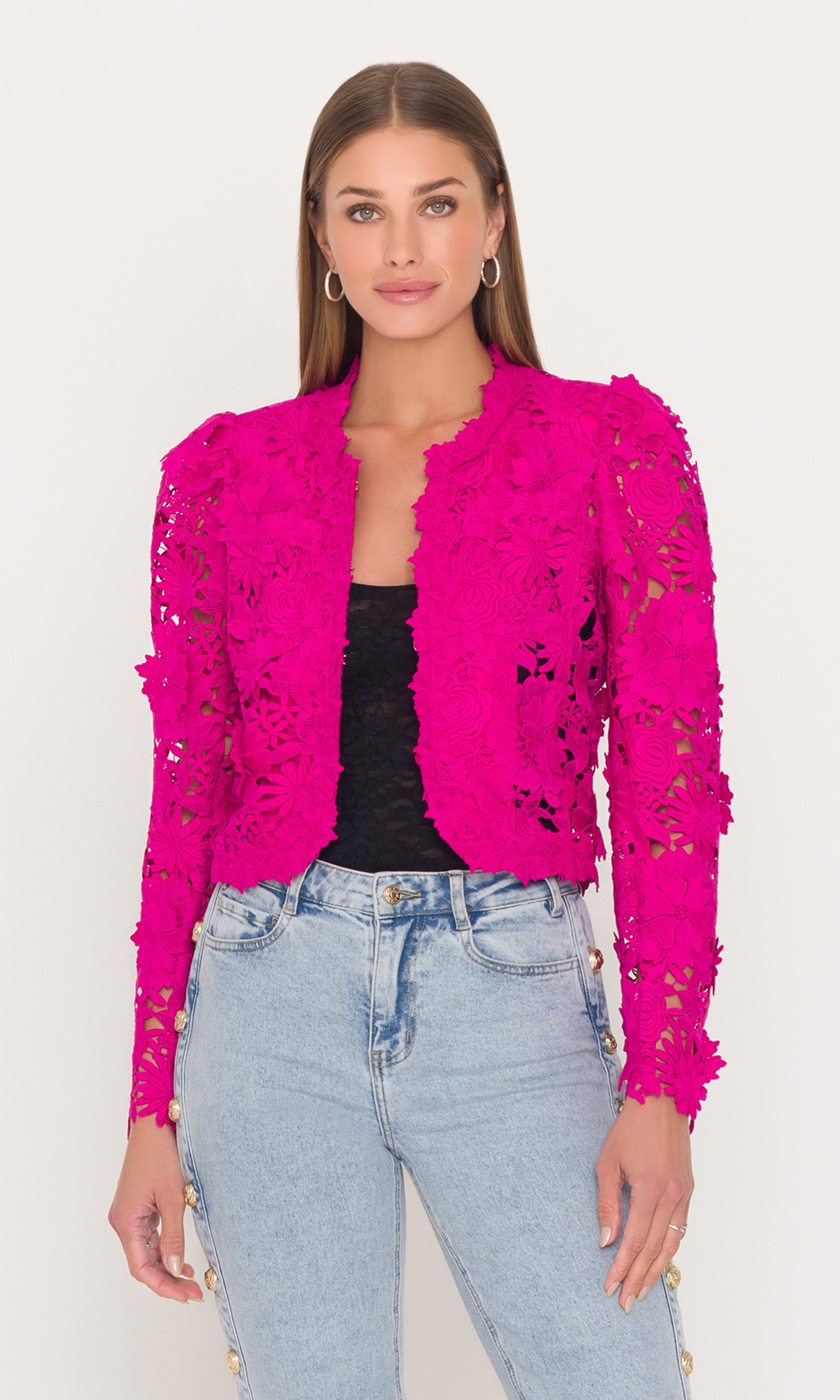 Woman wearing a bright pink lace jacket over a black top and blue jeans on a white background