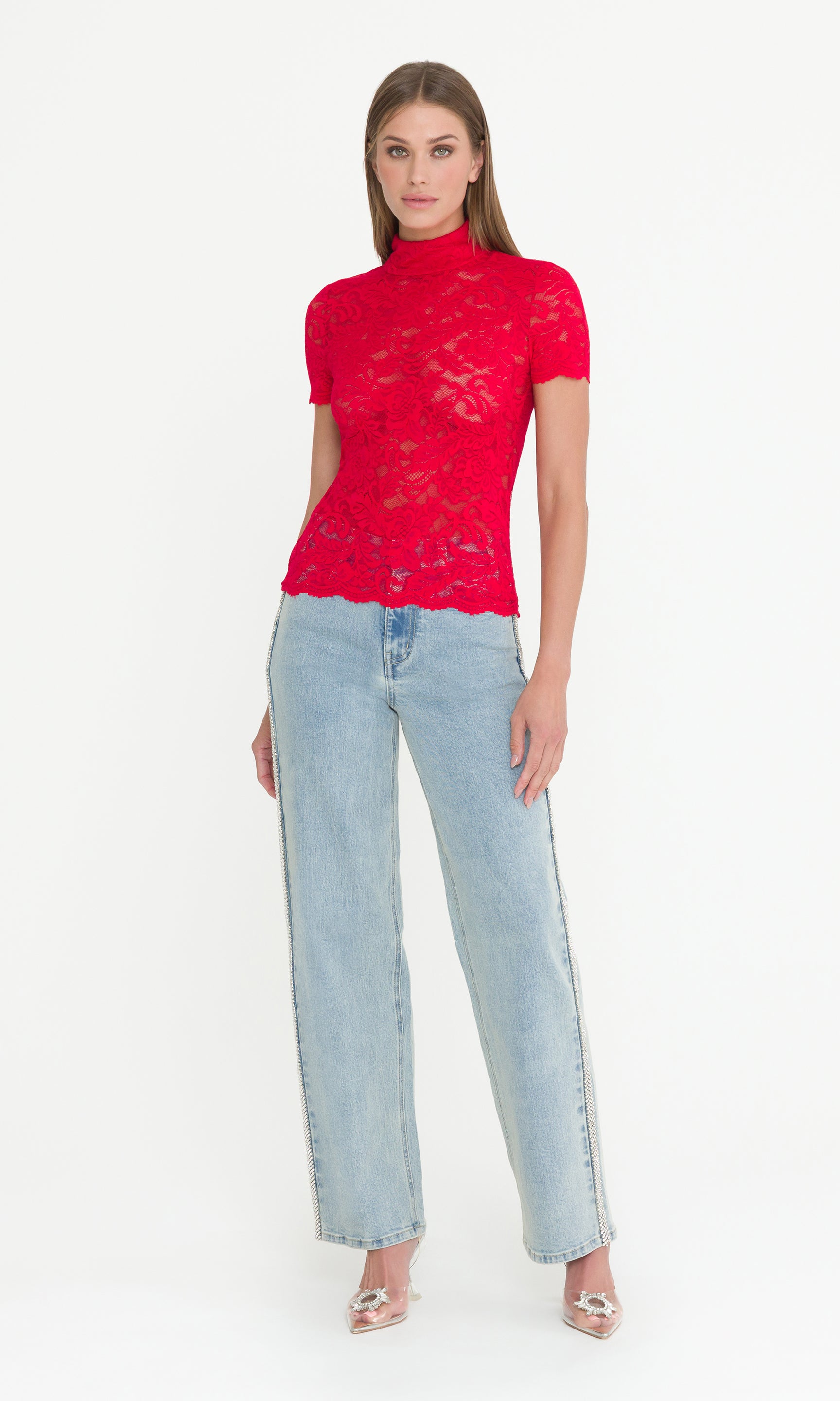 Full body image of woman wearing a red lace top and light blue jeans on a white background