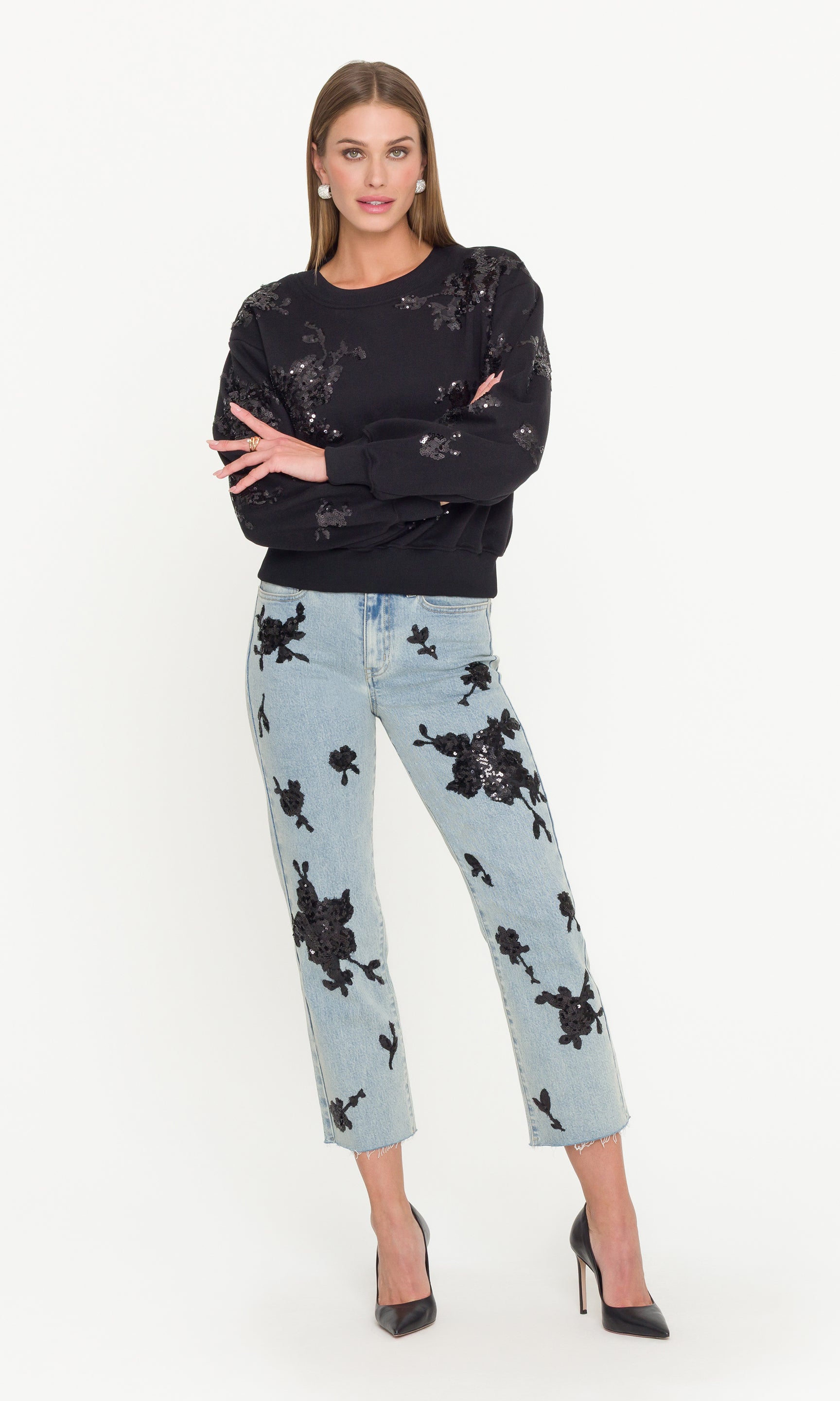 Woman wearing a black sequin sweatshirt and light blue jeans with black sequins on a white background