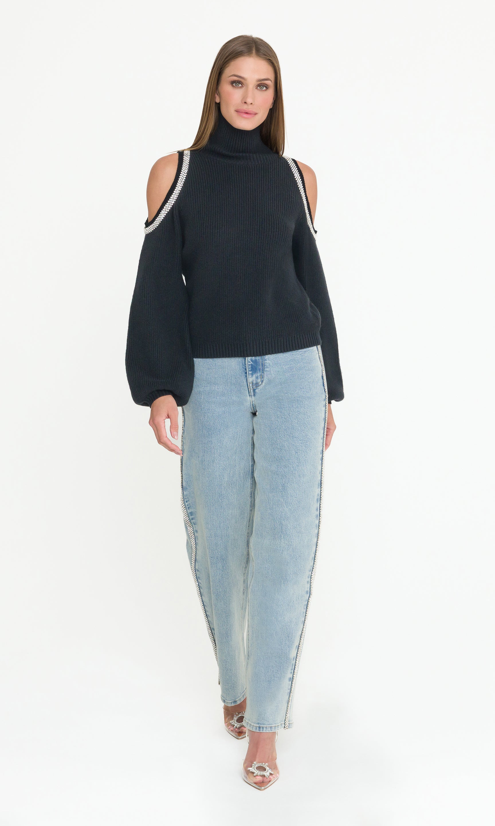 Woman wearing a black sweater with crystal shoulders and light blue jeans on a white background