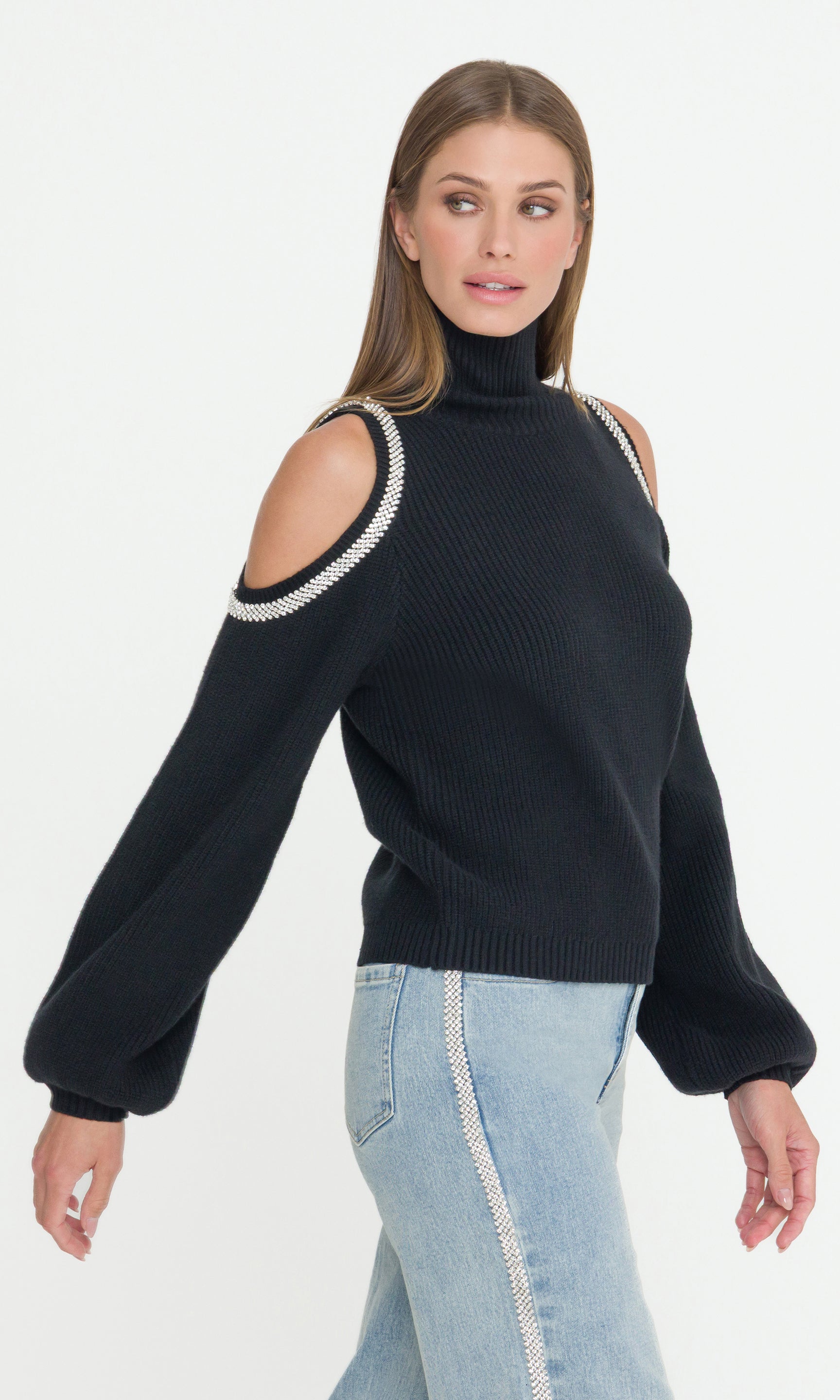 Side view of woman wearing a black sweater with cold shoulder design on a white background