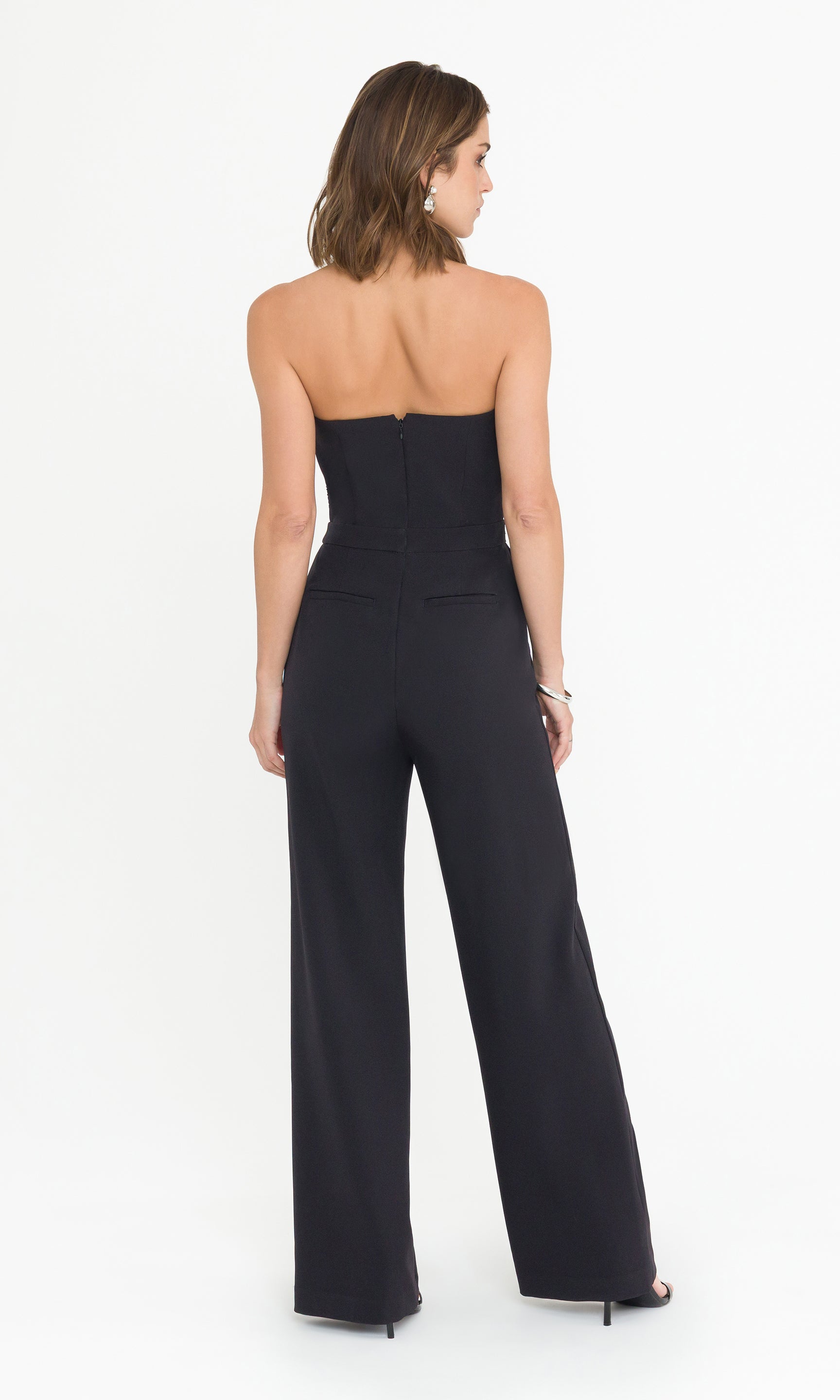 Back full body image of model wearing a black strapless jumpsuit on a white background
