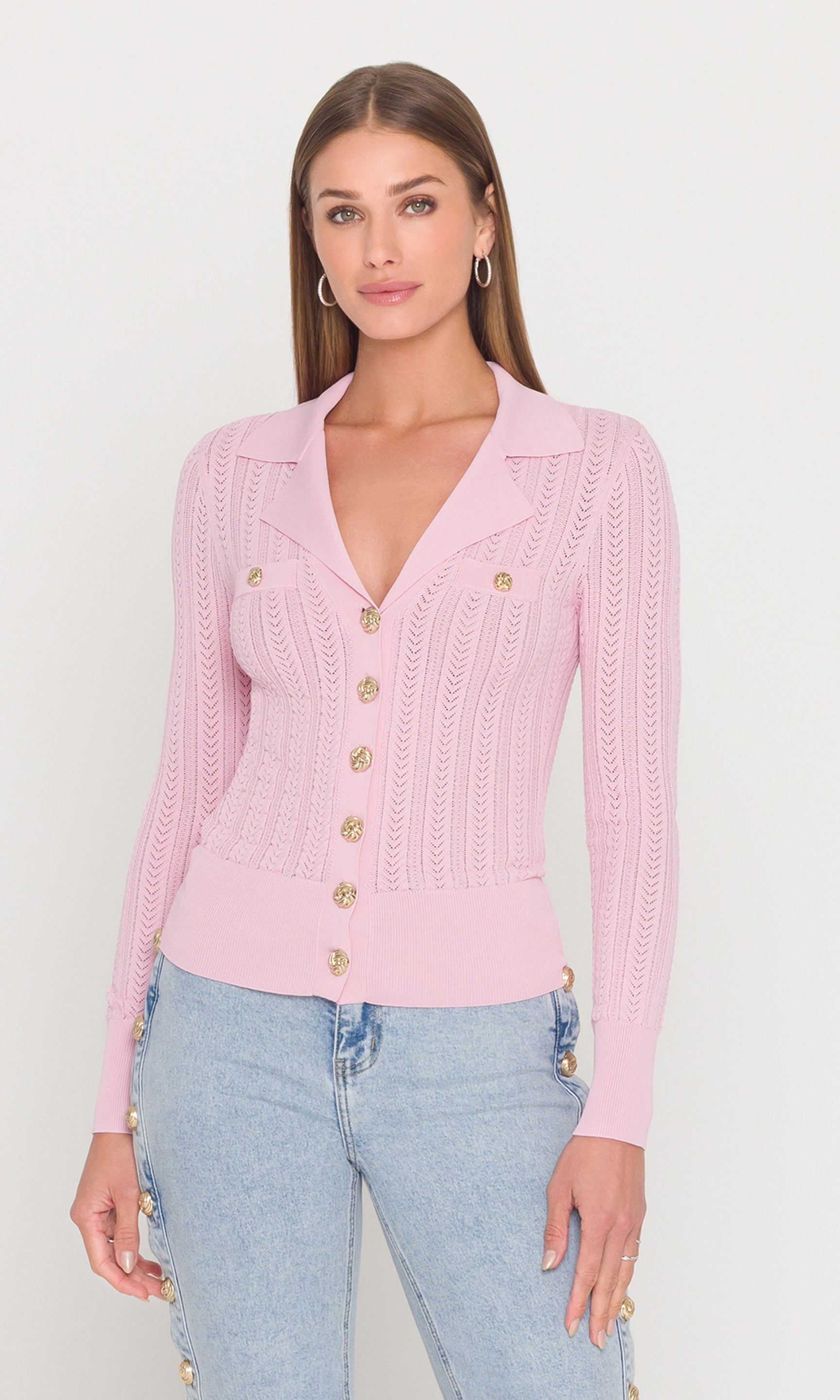 Woman wearing a pink cardigan with gold buttons on a white background