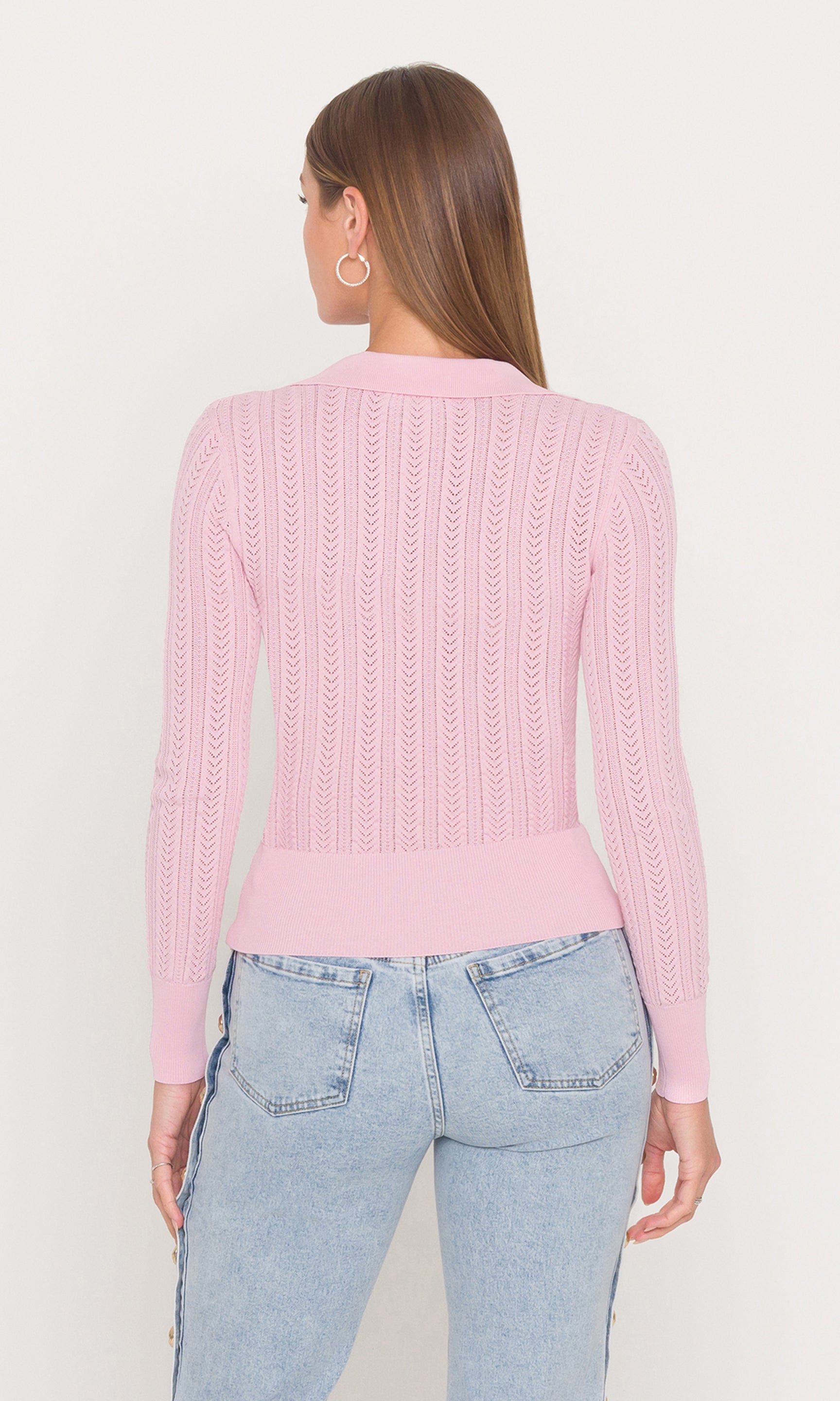 Back view of woman wearing a pink knitted sweater and light blue jeans on a white background