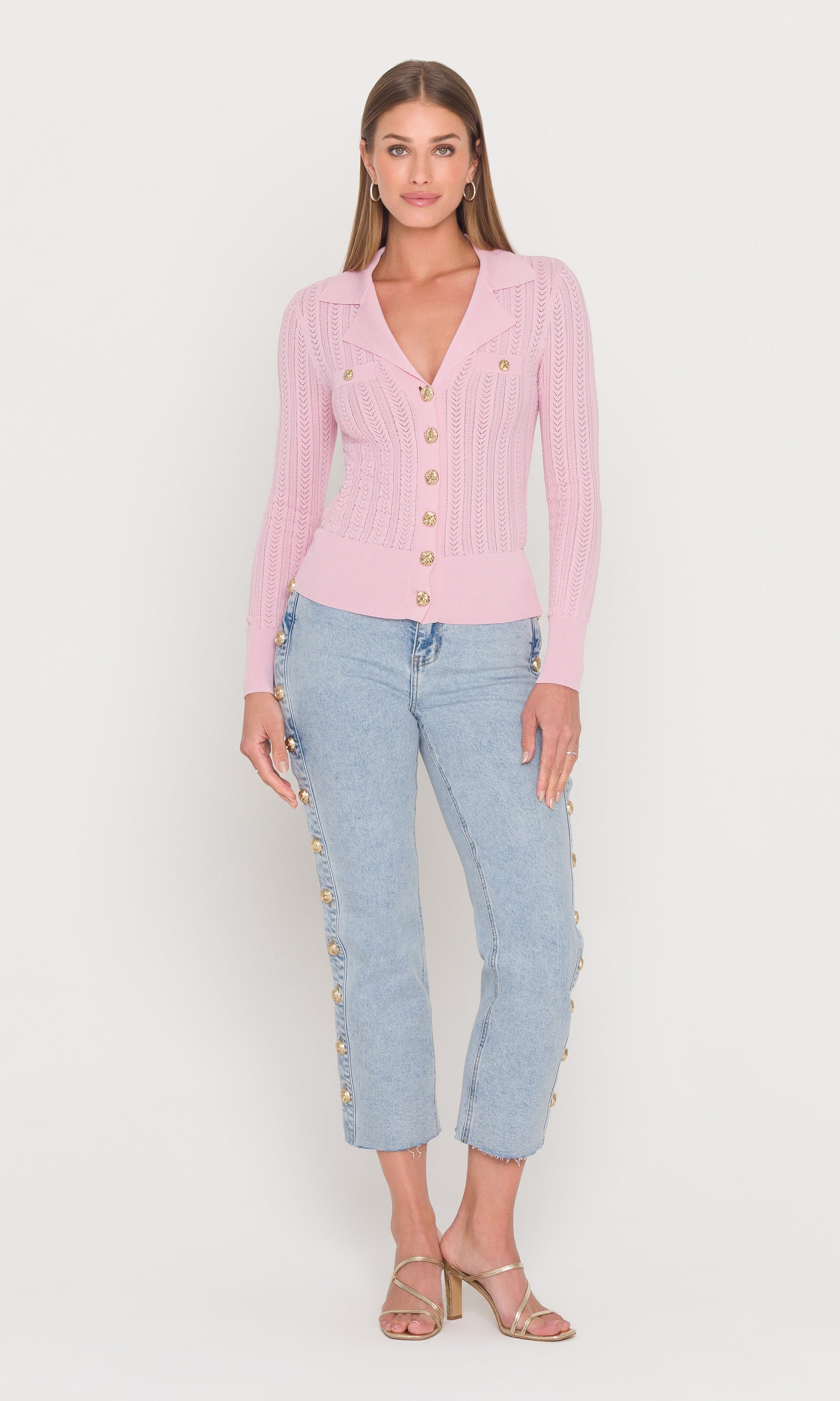 Full body image of woman wearing a pink cardigan and light blue jeans on a white background