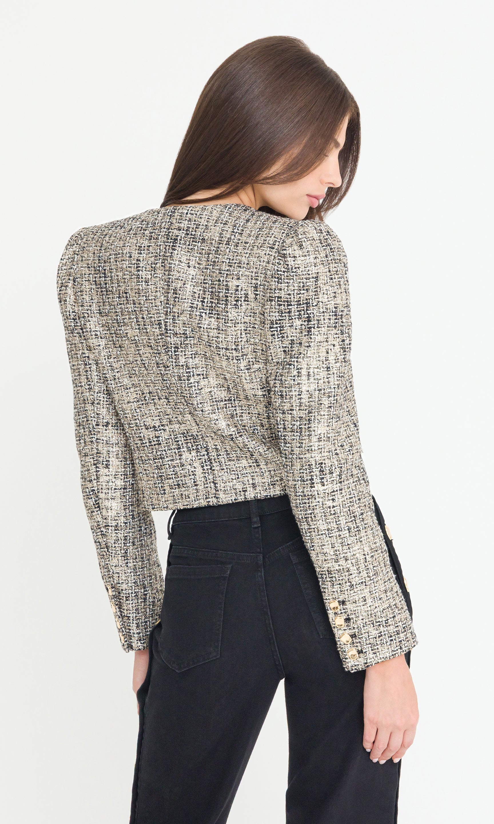 Back view of Woman wearing a gold multi tweed jacket with black jeans on a white background
