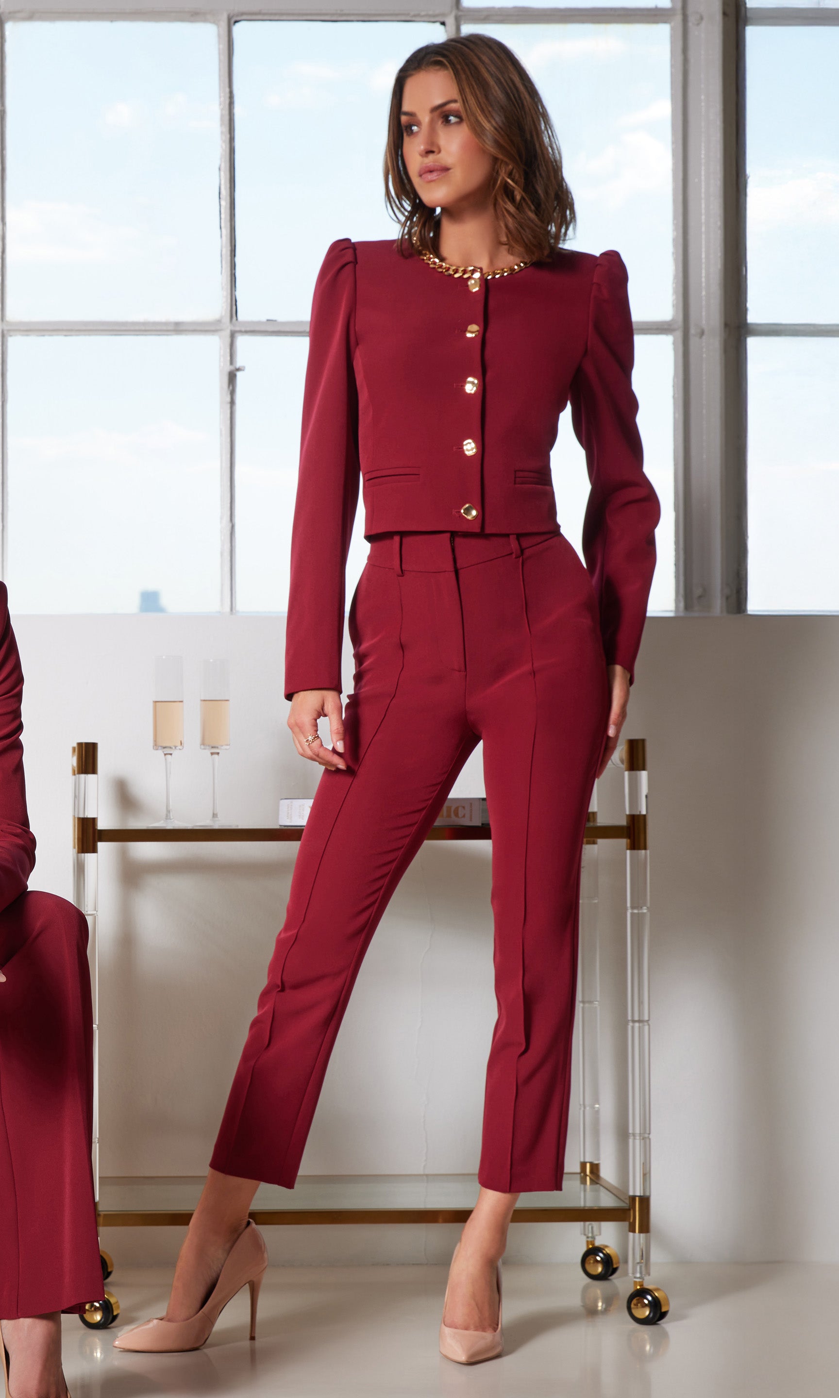 Woman wearing a red suit with gold buttons in a room with large windows.