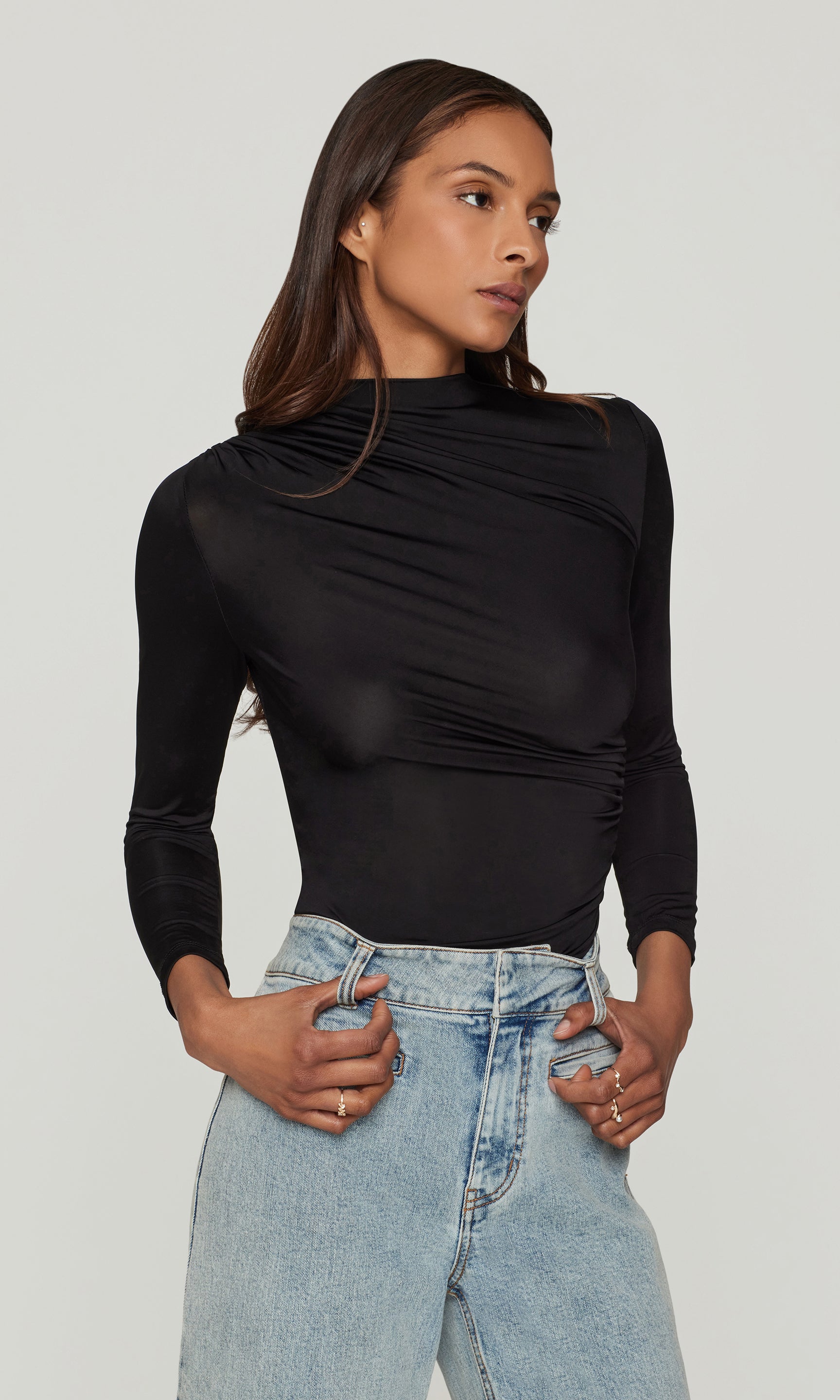 Side view of woman wearing a black long-sleeve top and light blue jeans on a plain background