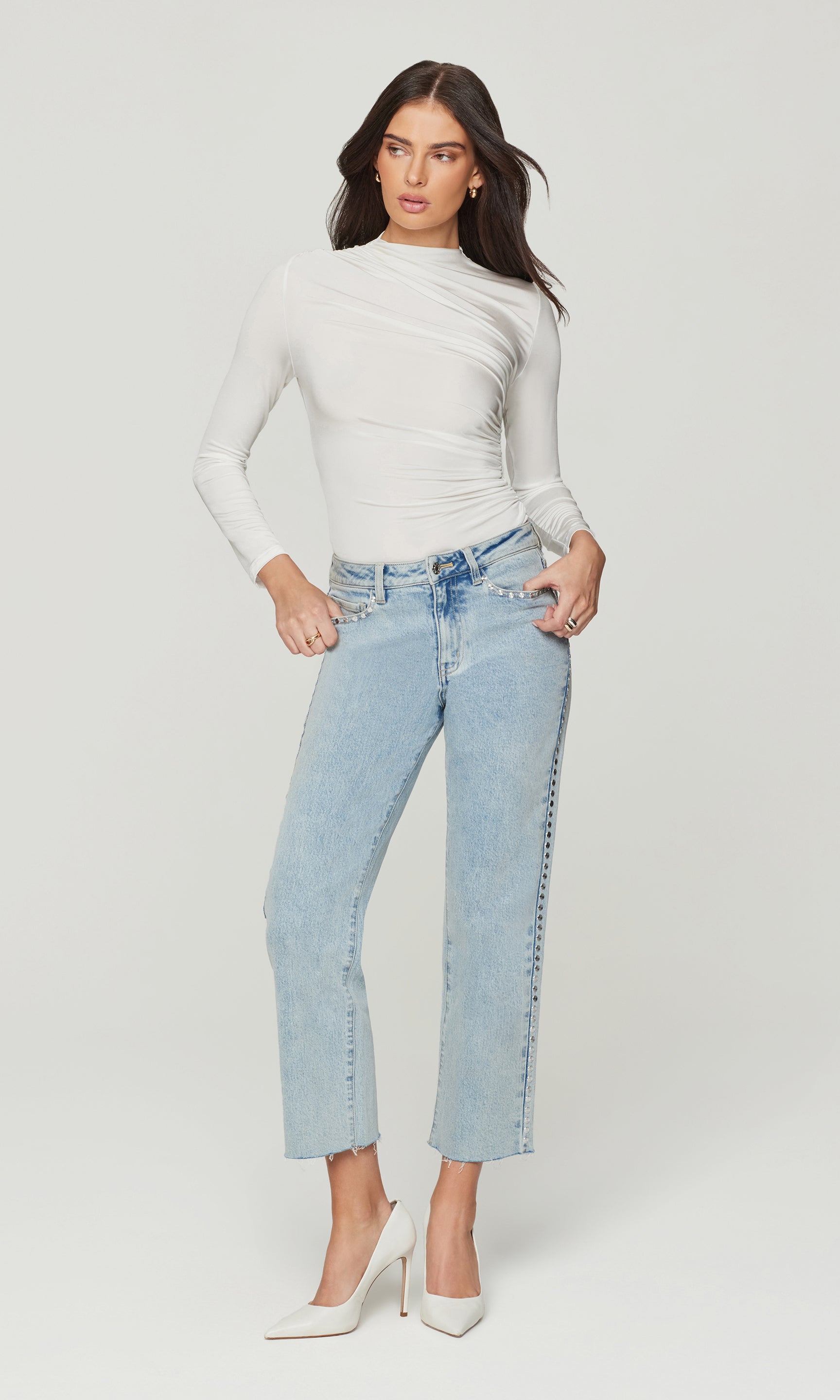 Woman wearing a white long-sleeve top and light blue jeans on a plain background