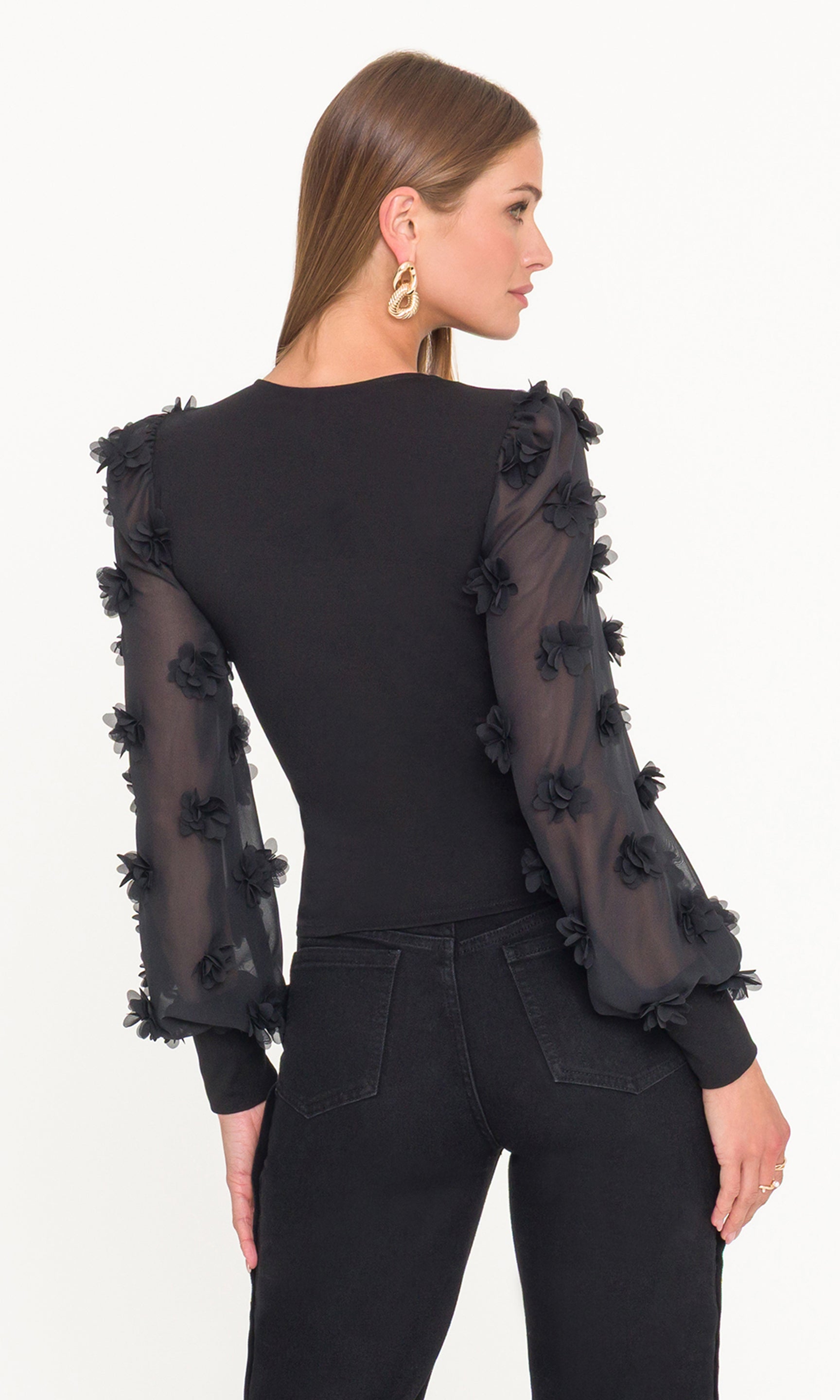 Black outfit with sheer sleeves featuring floral appliqués on a white background
