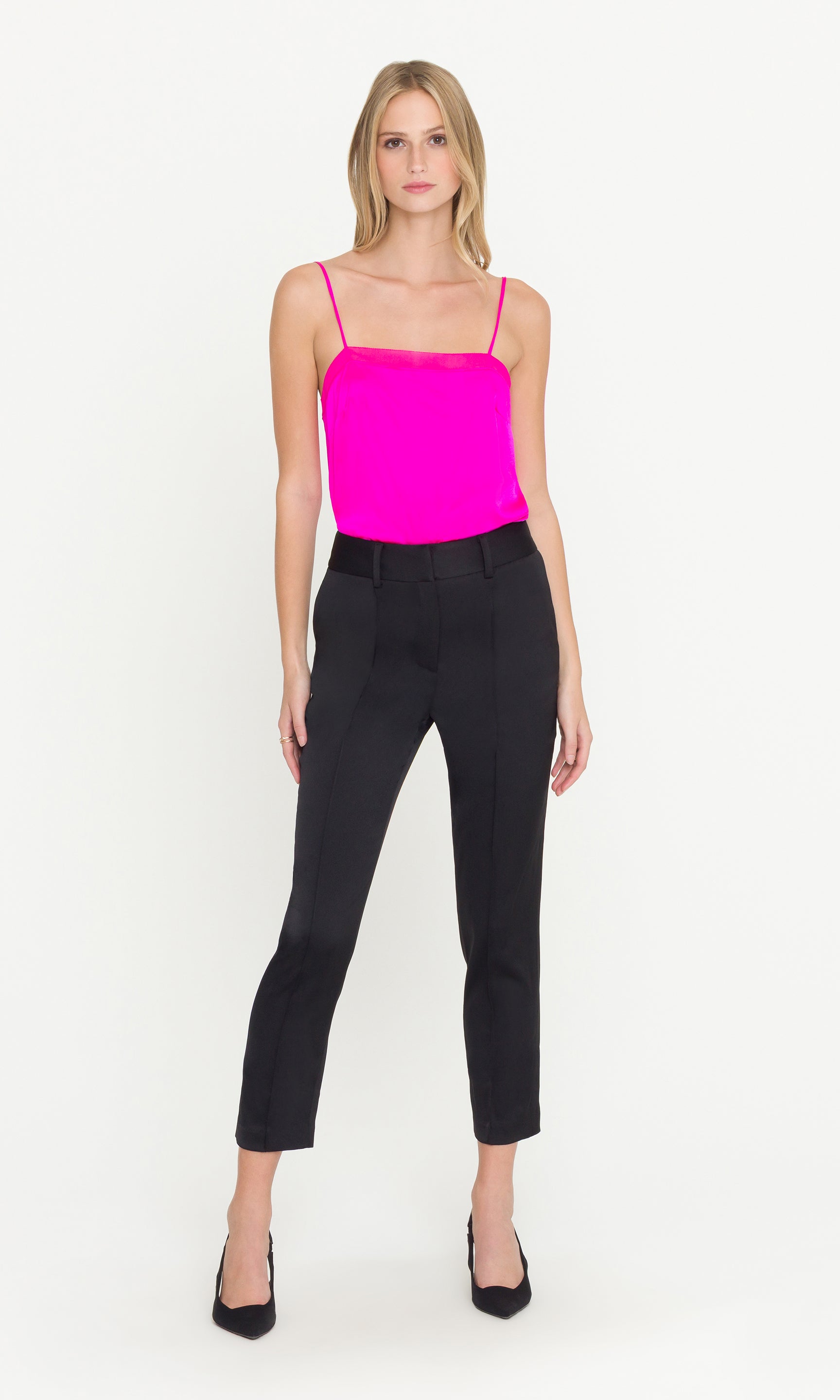 Woman wearing a bright pink top and black pants on a white background