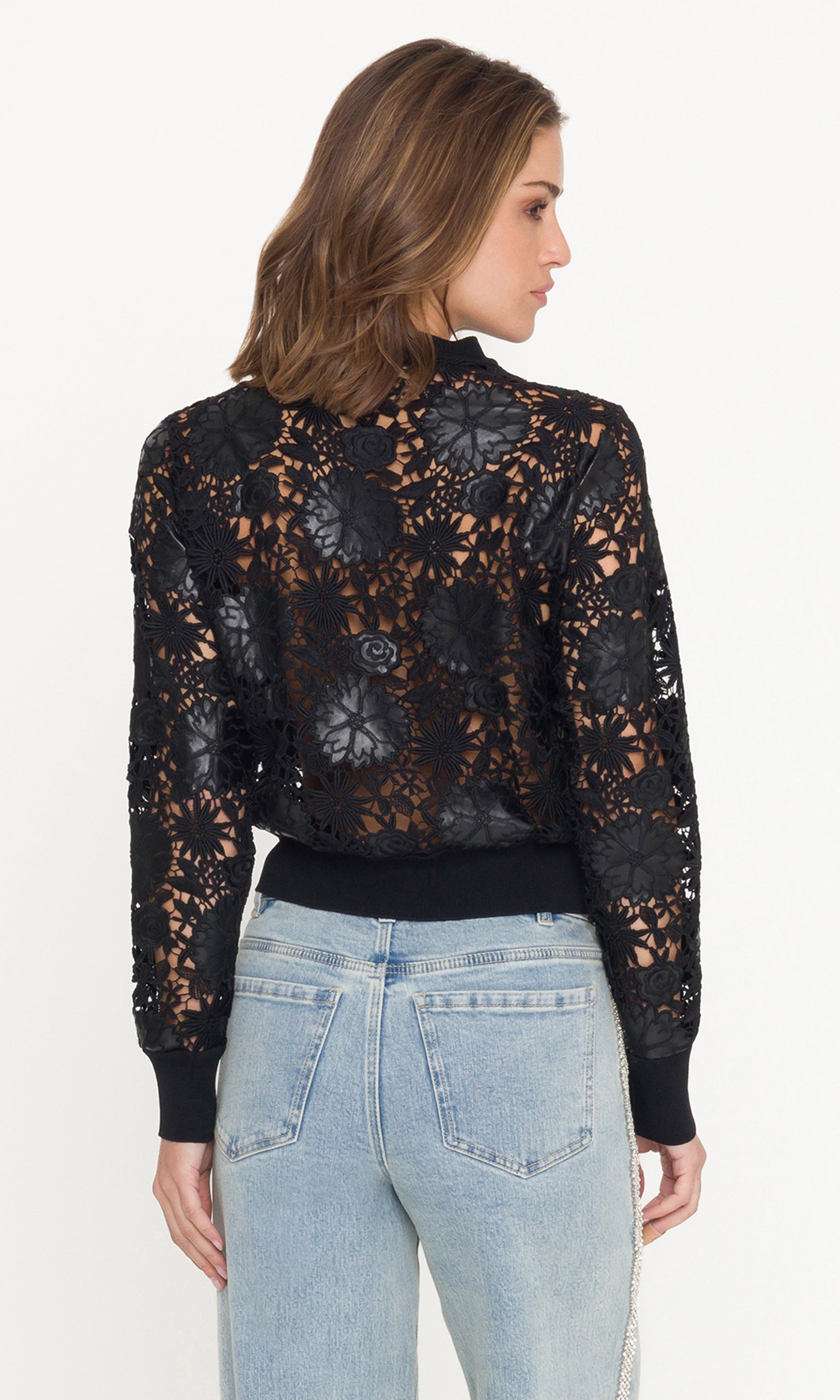 Woman wearing a black lace cardigan and light blue jeans on a white background