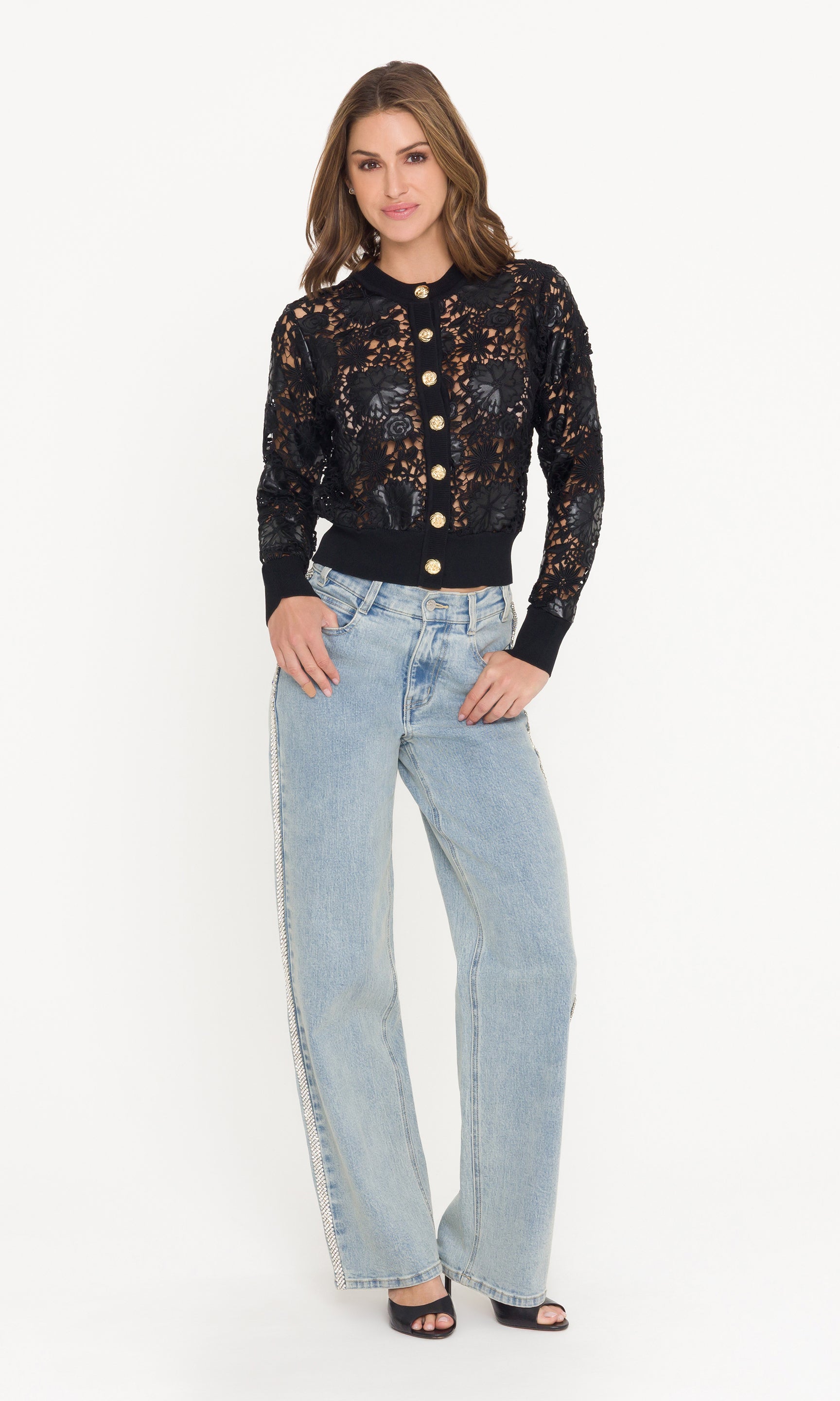 Woman wearing a black lace cardigan with gold buttons and light blue jeans on a white background