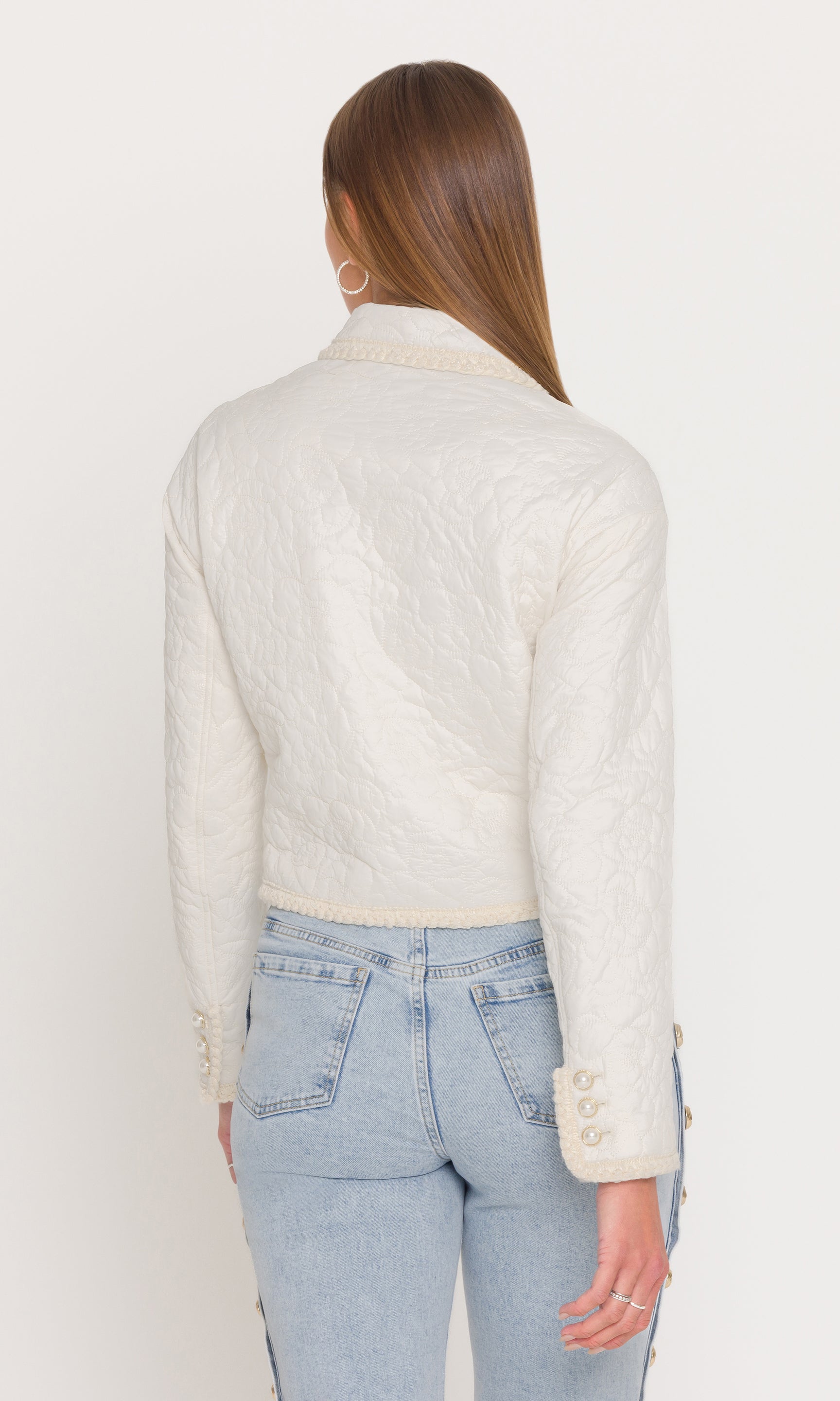 Back view of woman wearing a white textured jacket and light blue jeans on a white background
