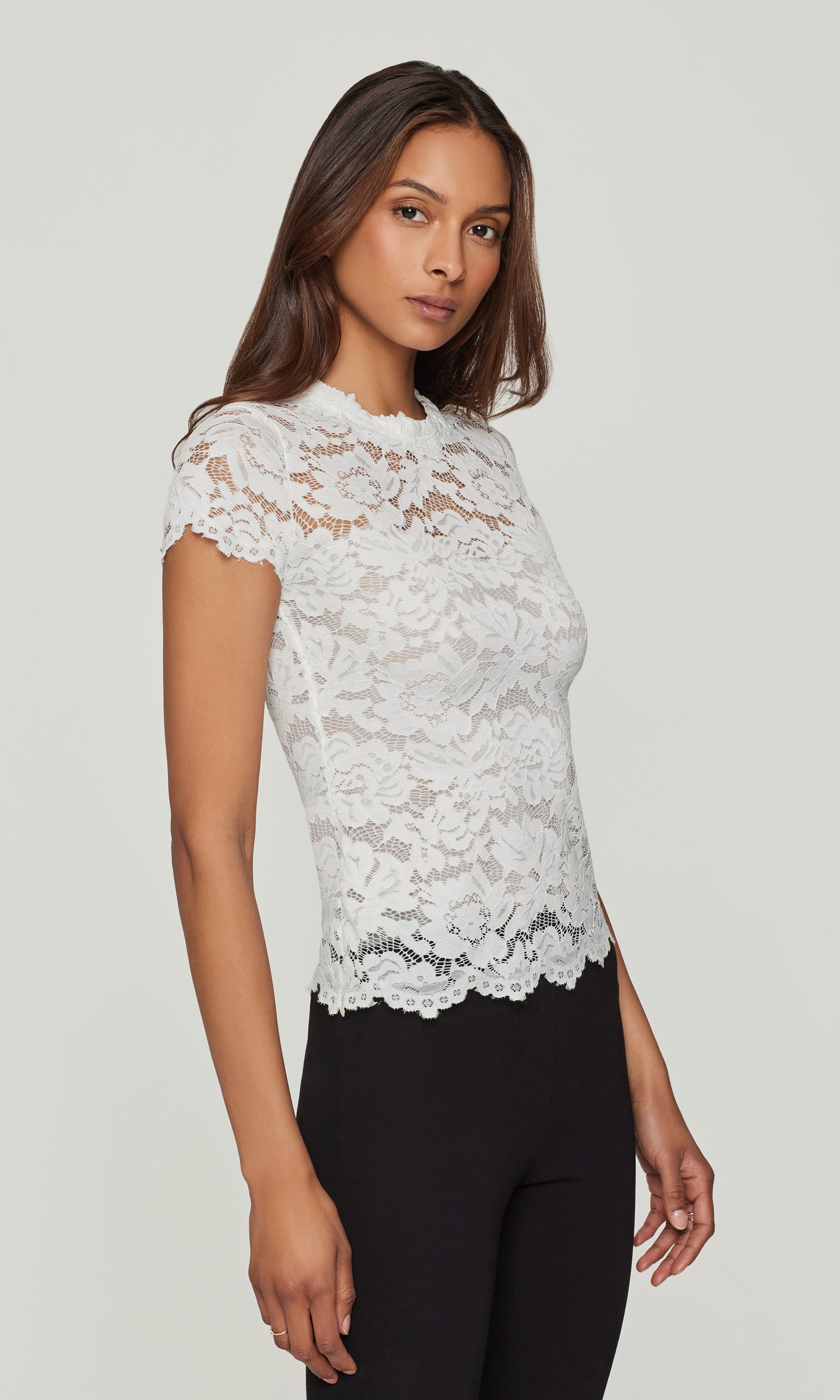 Side view of woman wearing a white lace top against a plain background