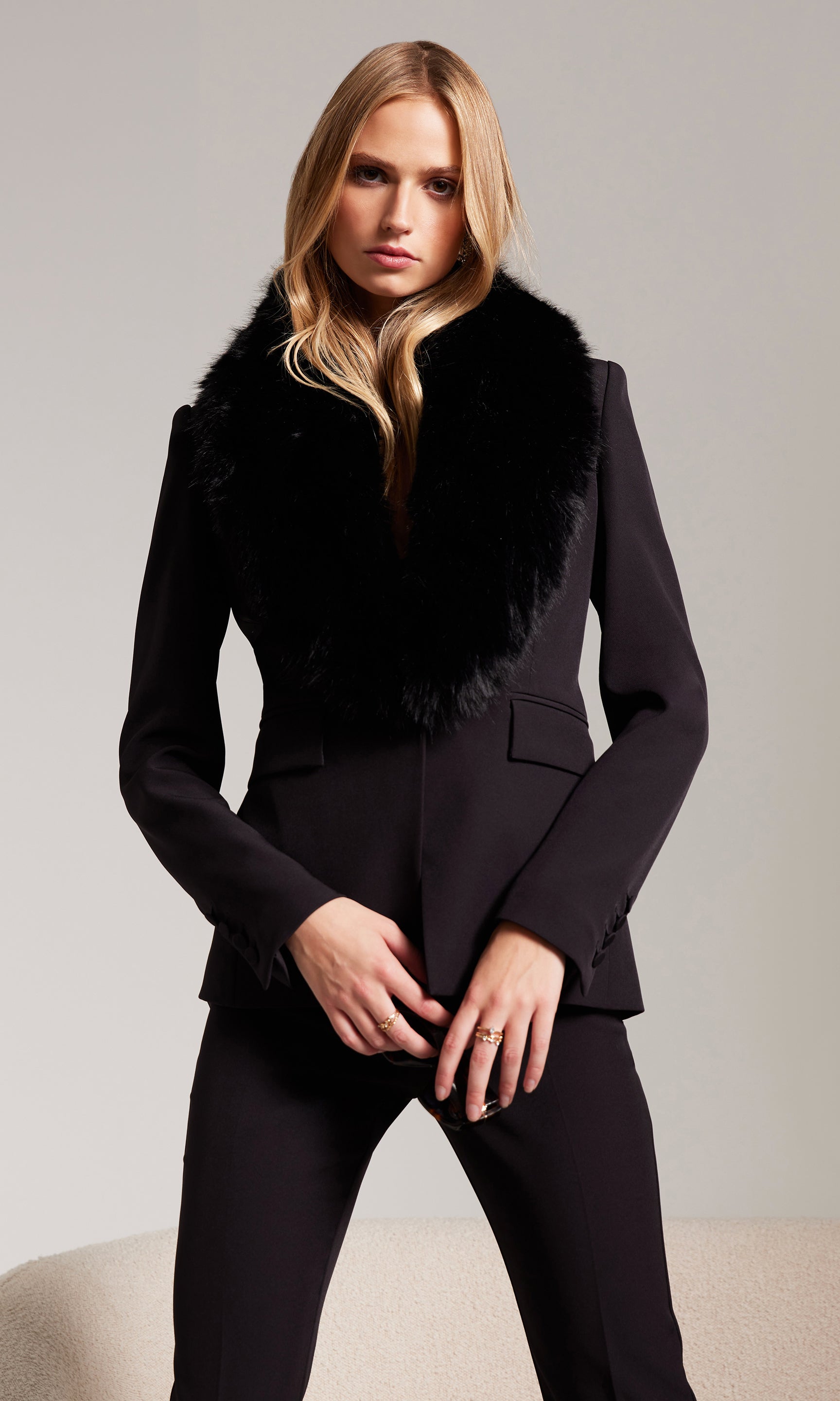Woman wearing a black coat with fur collar against a plain background