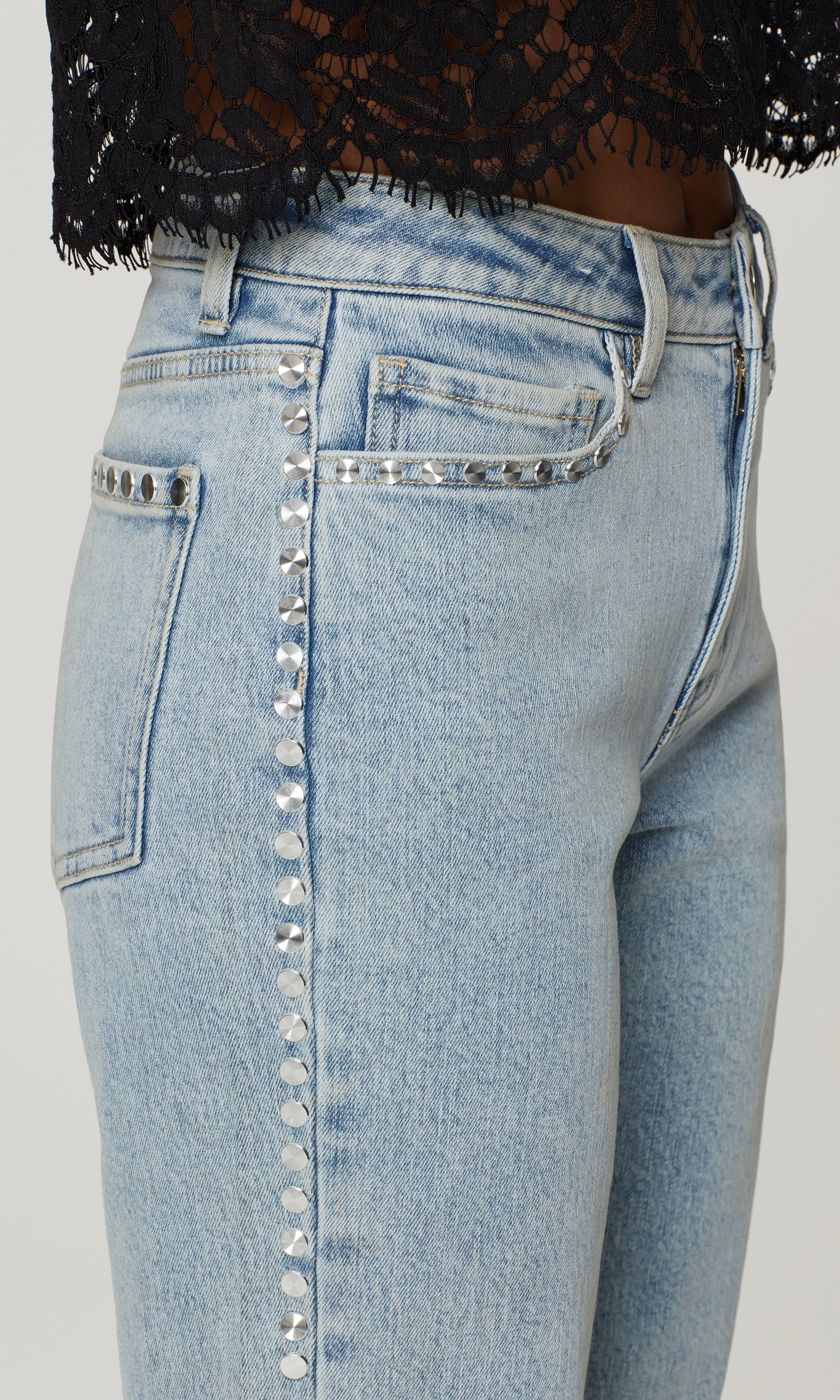 Light blue jeans with decorative studs on a gray background