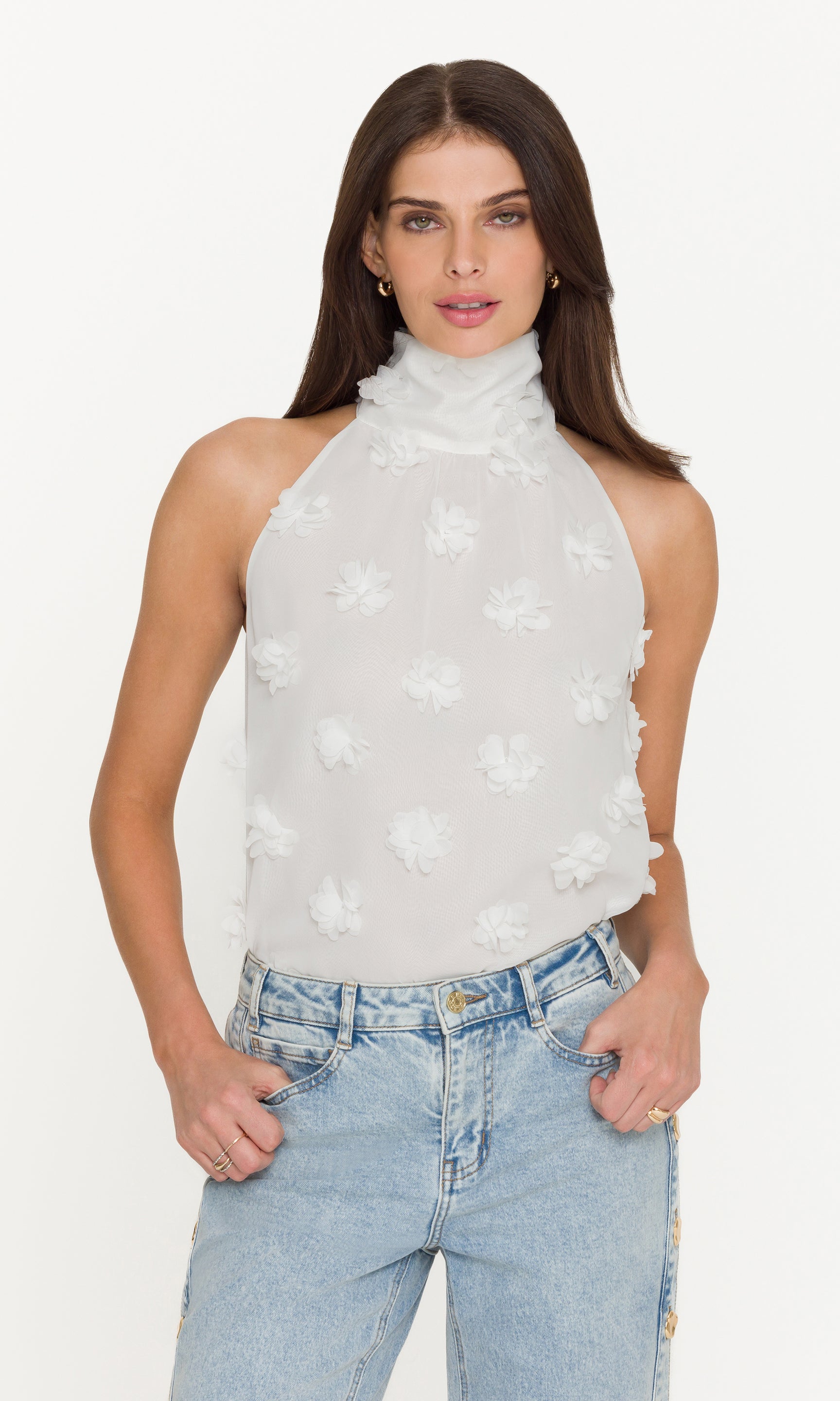 Woman wearing a white sleeveless top with floral patterns and light blue jeans on a white background