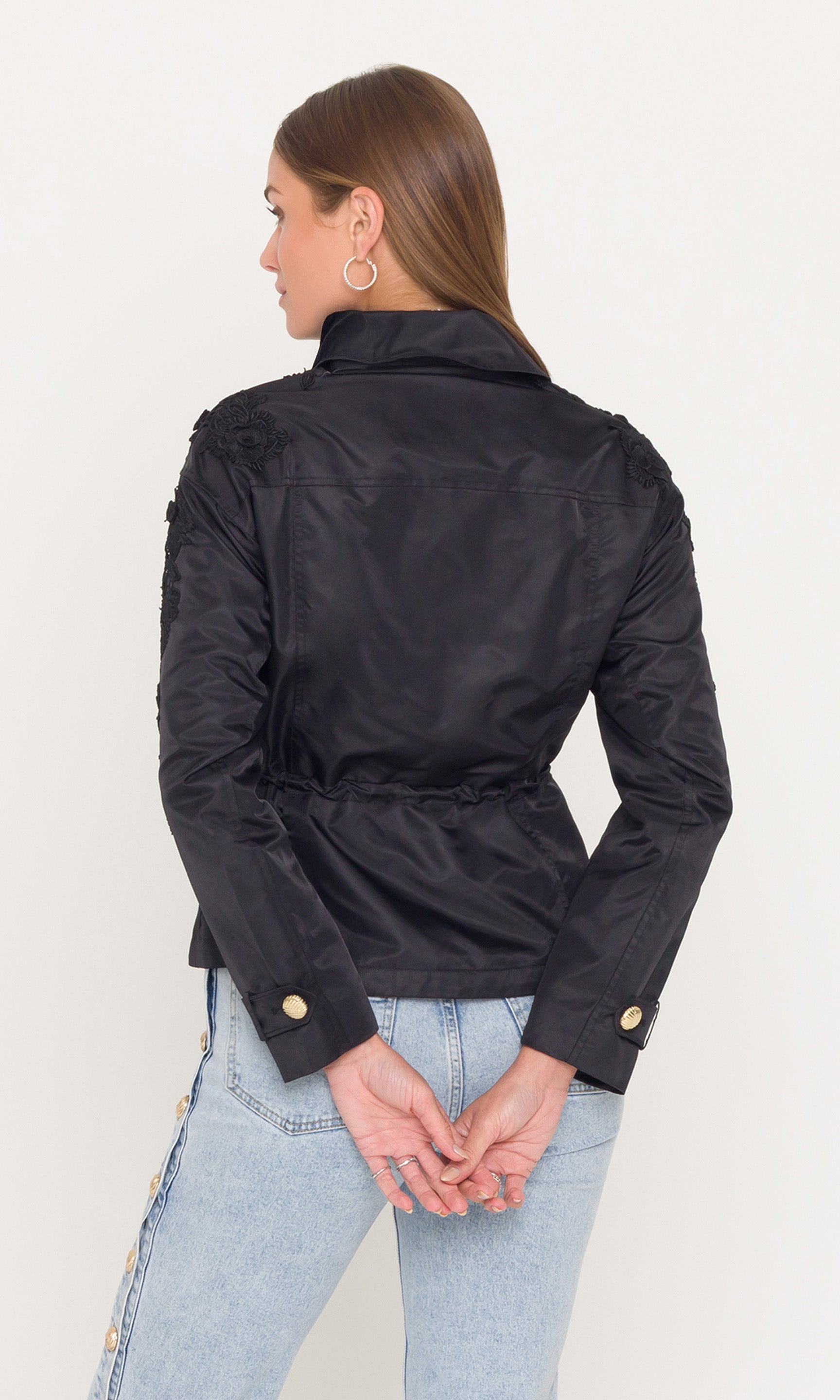 Back view of person wearing a black parka jacket and light blue jeans on a white background