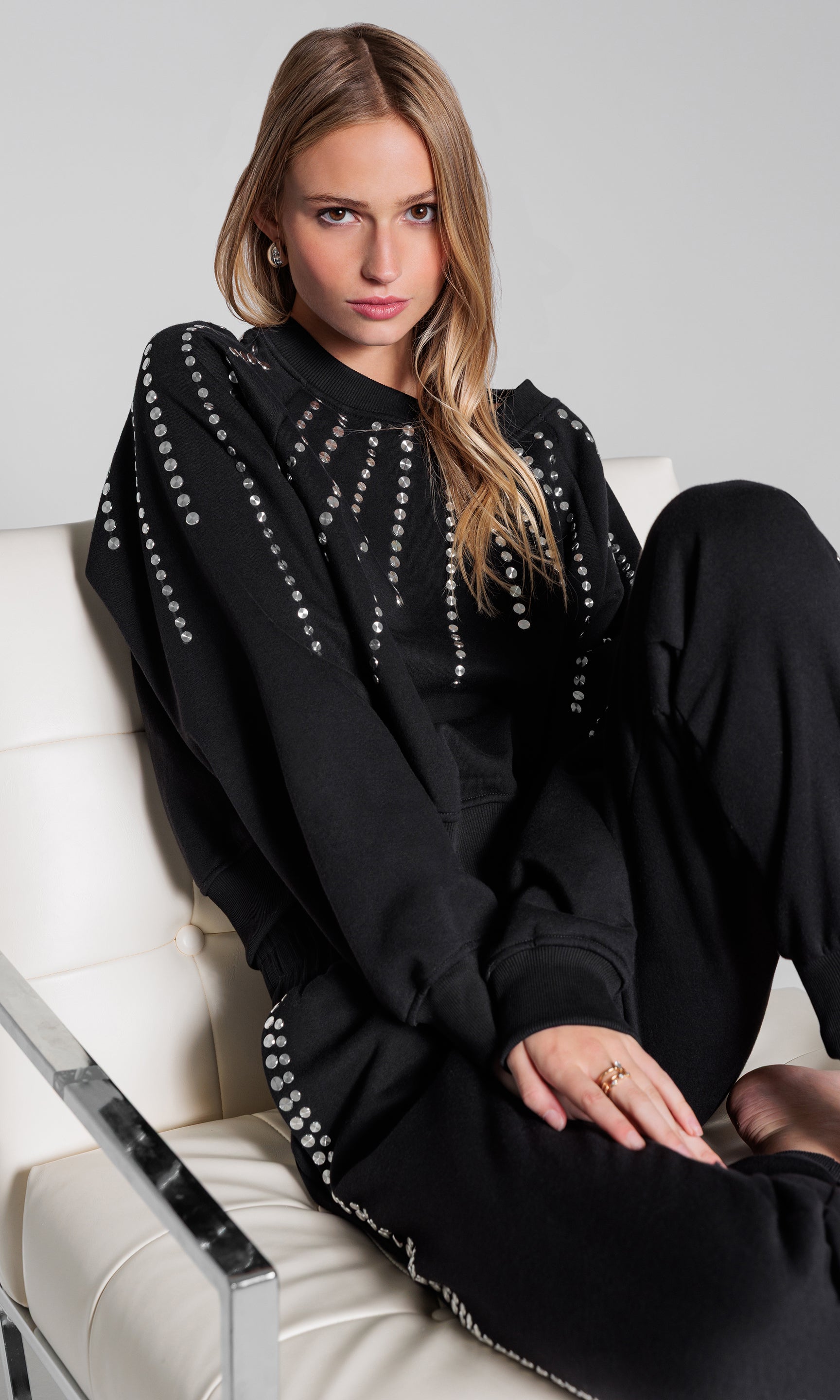 Woman wearing a black outfit with white embellishments sitting on a white chair.