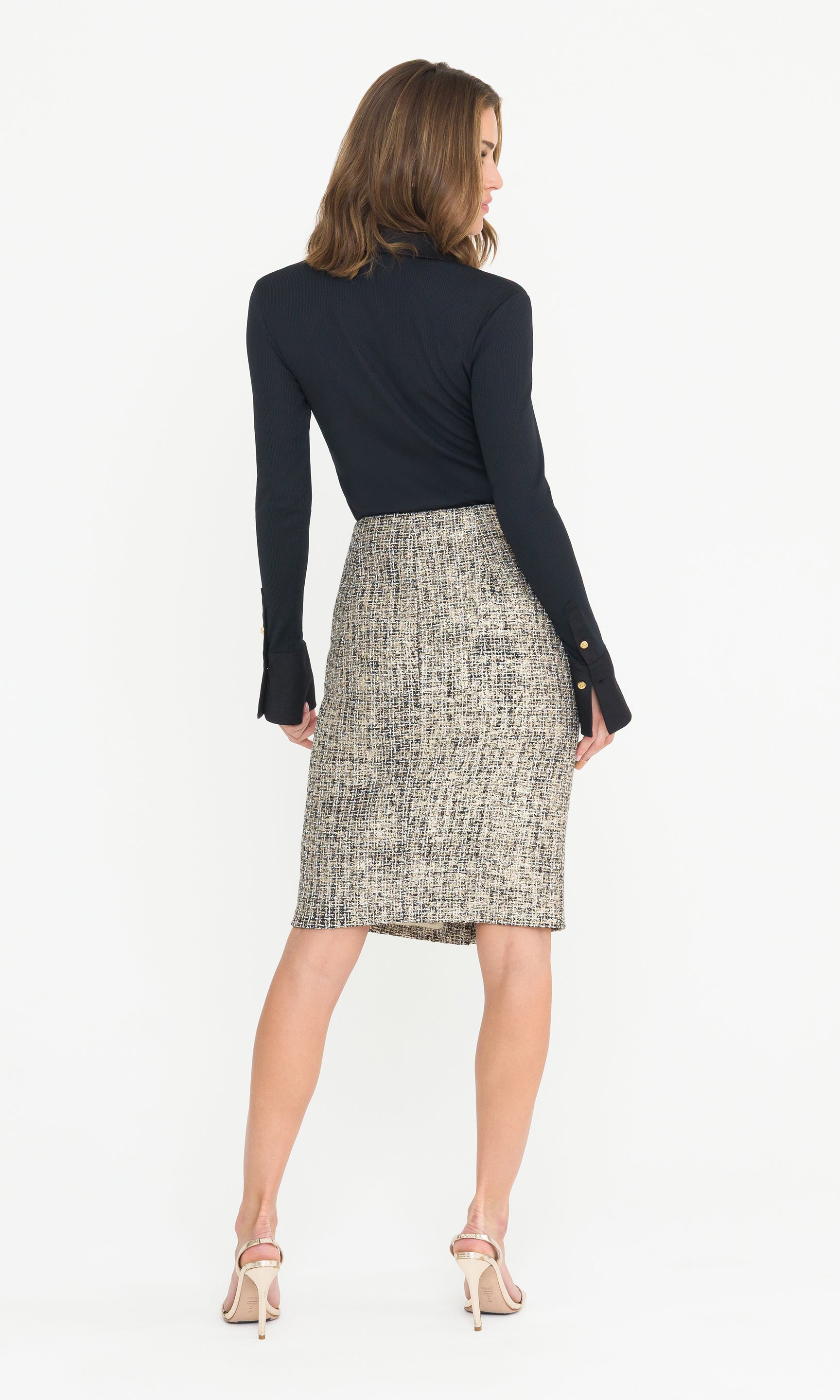 Back view full body image of model wearing a black top and a gold patterned tweed skirt