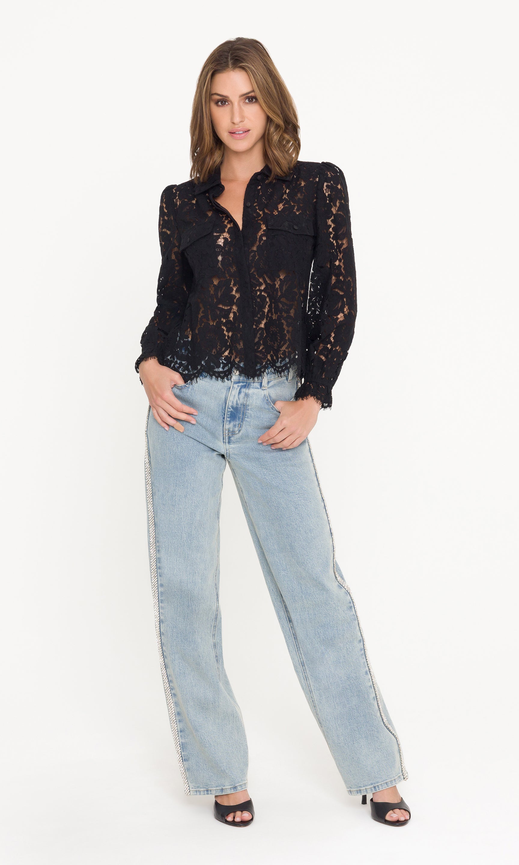 Woman wearing a black lace blouse and light blue jeans on a white background