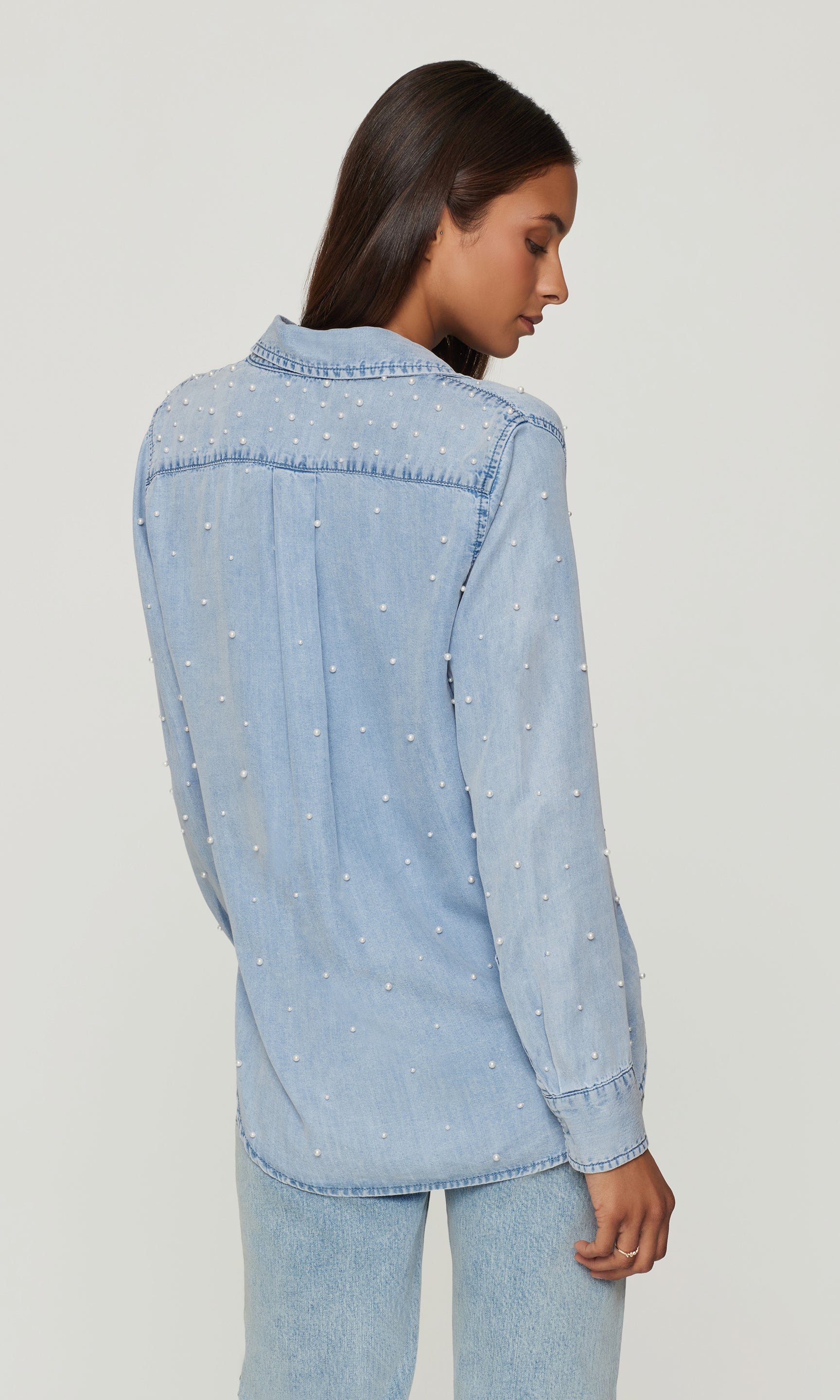 Woman wearing a light blue denim shirt against a plain background