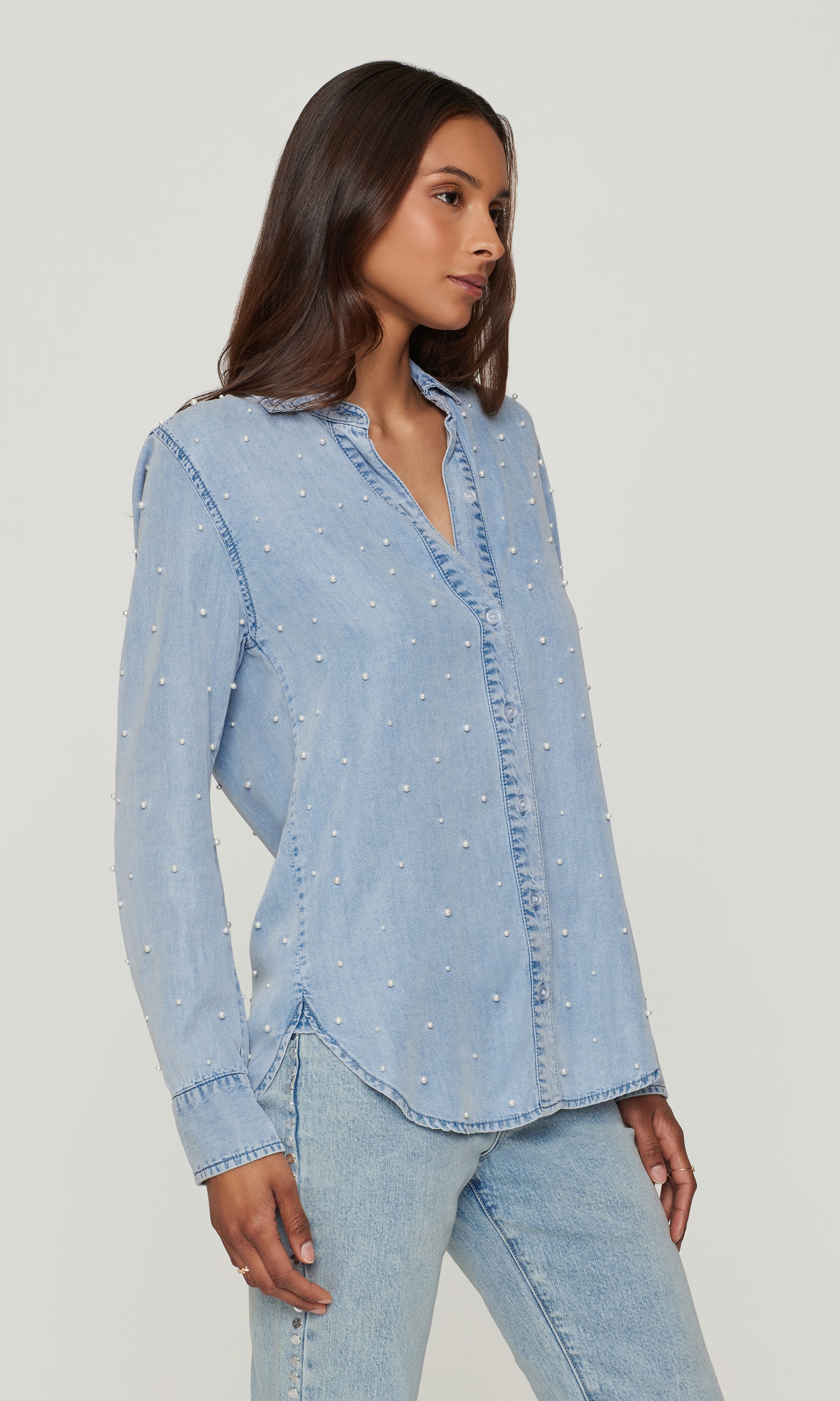 Woman wearing a light blue denim shirt and jeans on a plain background