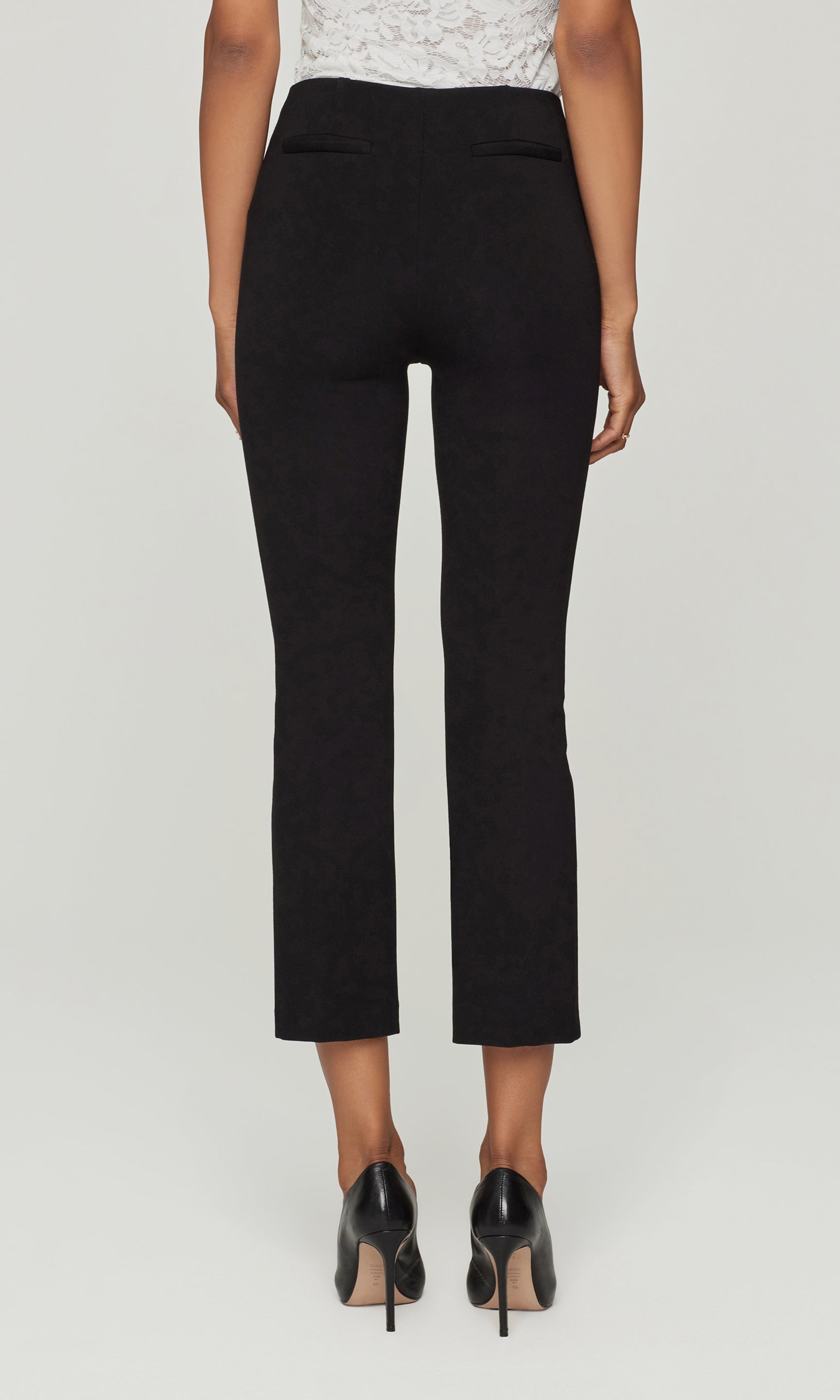 Back view of person wearing black pants on a light gray background