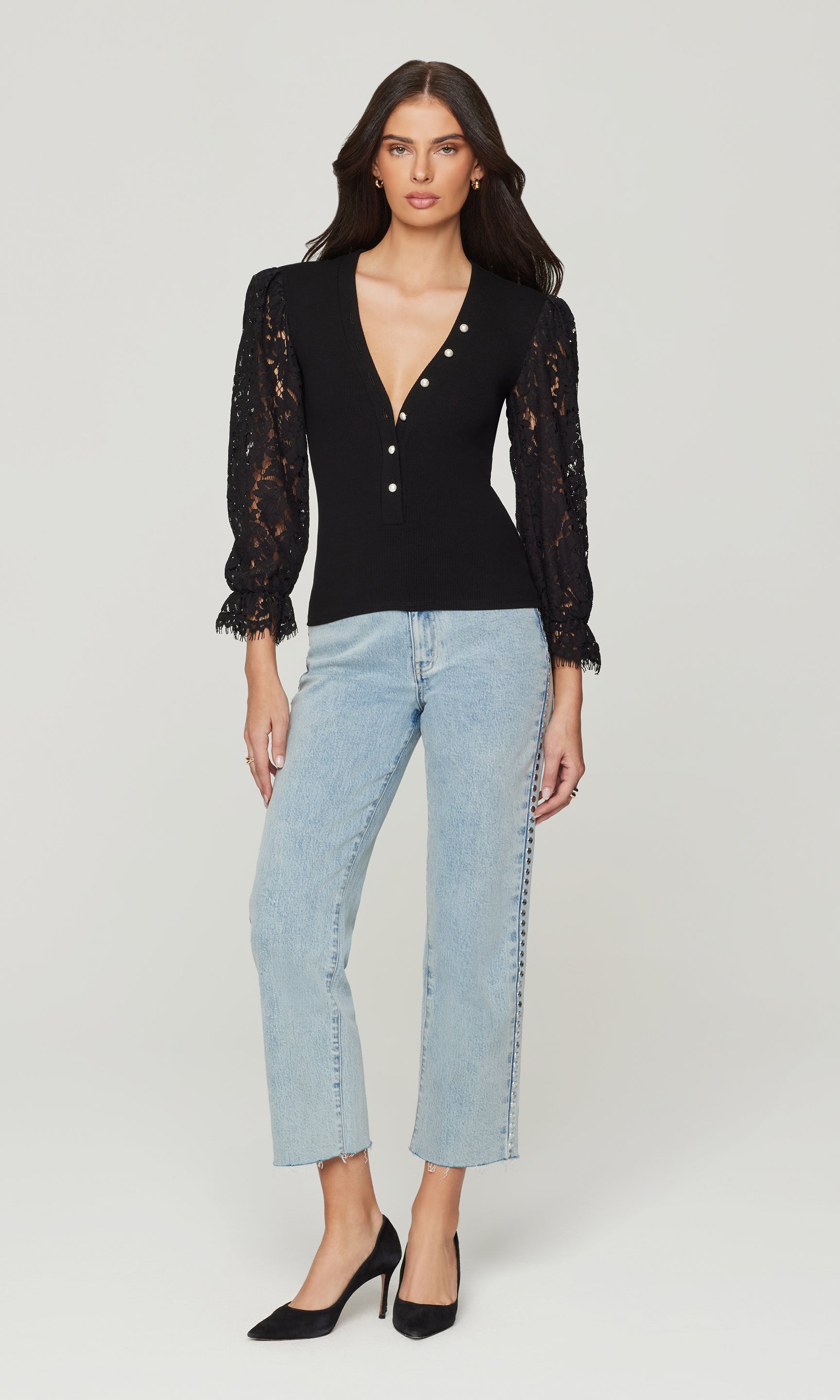 Woman wearing a black lace top and light blue jeans on a white background