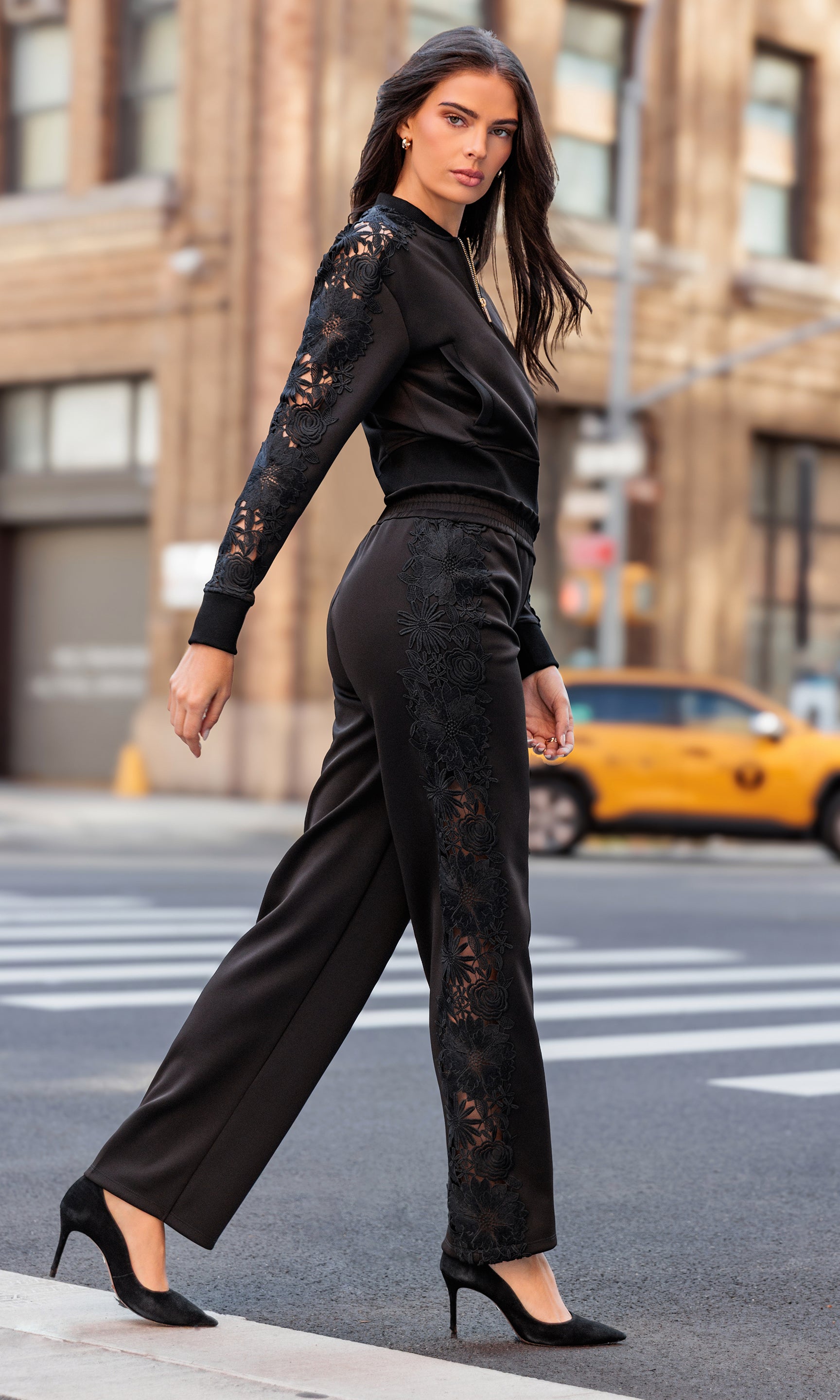Woman in a black lace outfit walking on a city street with a taxi in the background.
