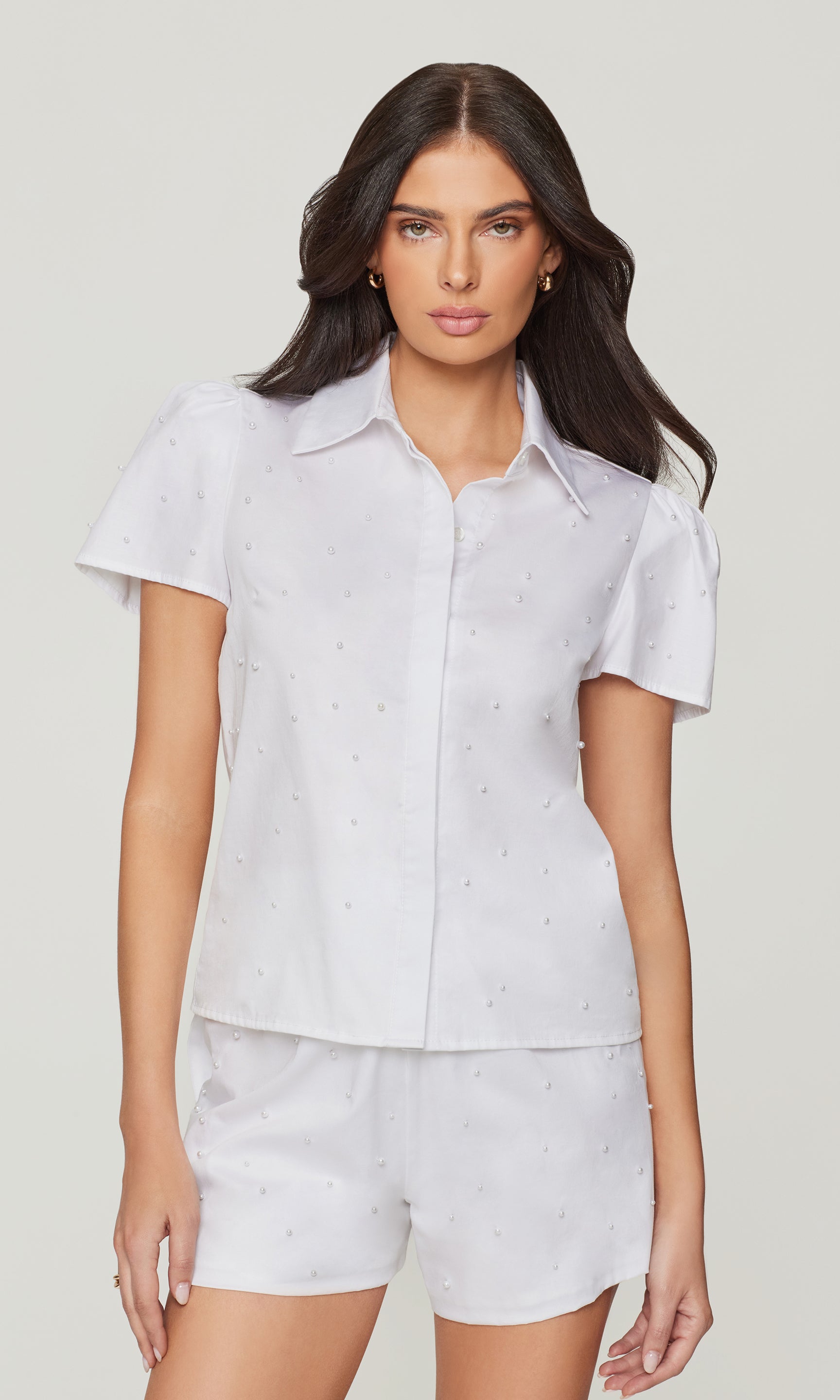 Woman wearing a white short-sleeve shirt and shorts set on a plain background