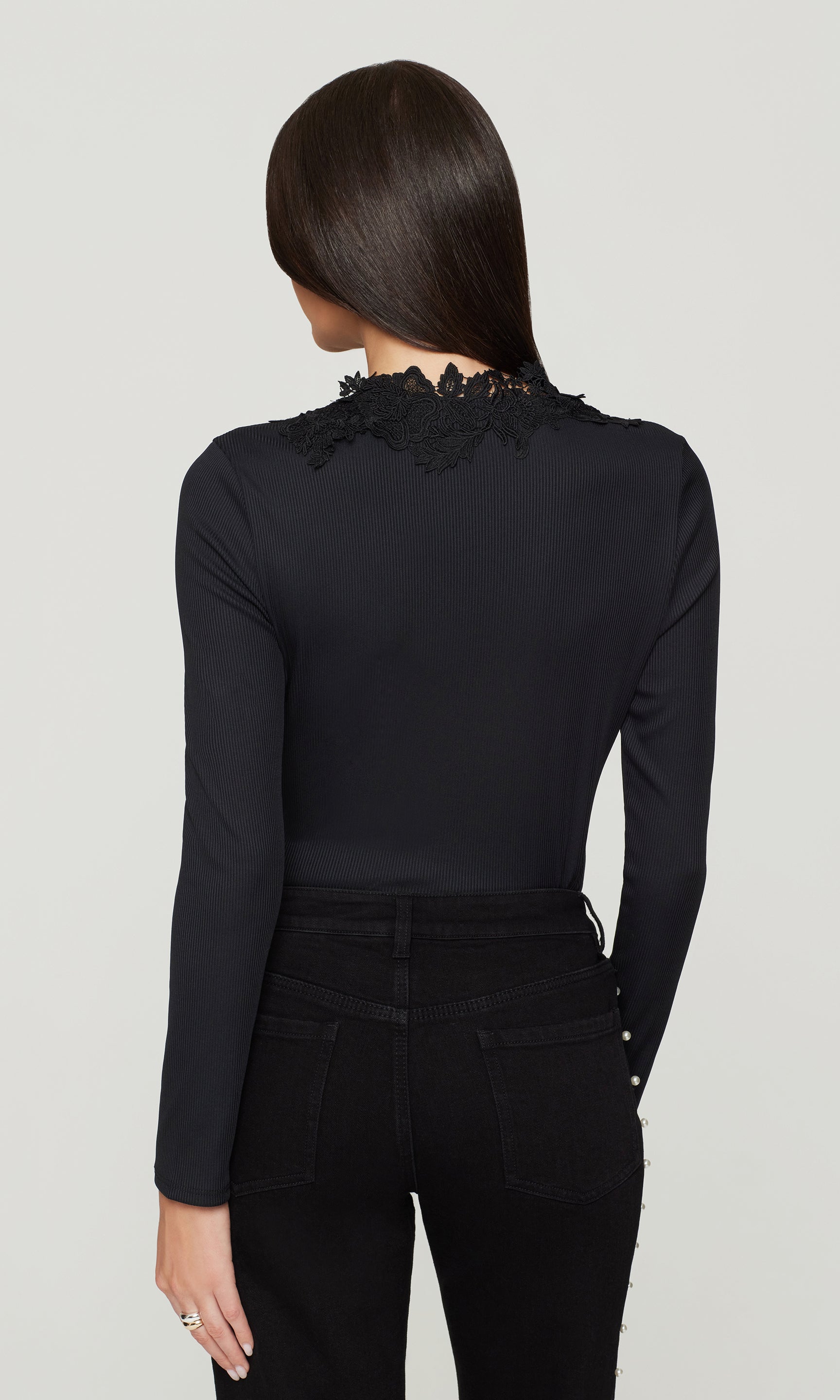 Back view of model wearing a black long-sleeve top with lace details on a light gray background