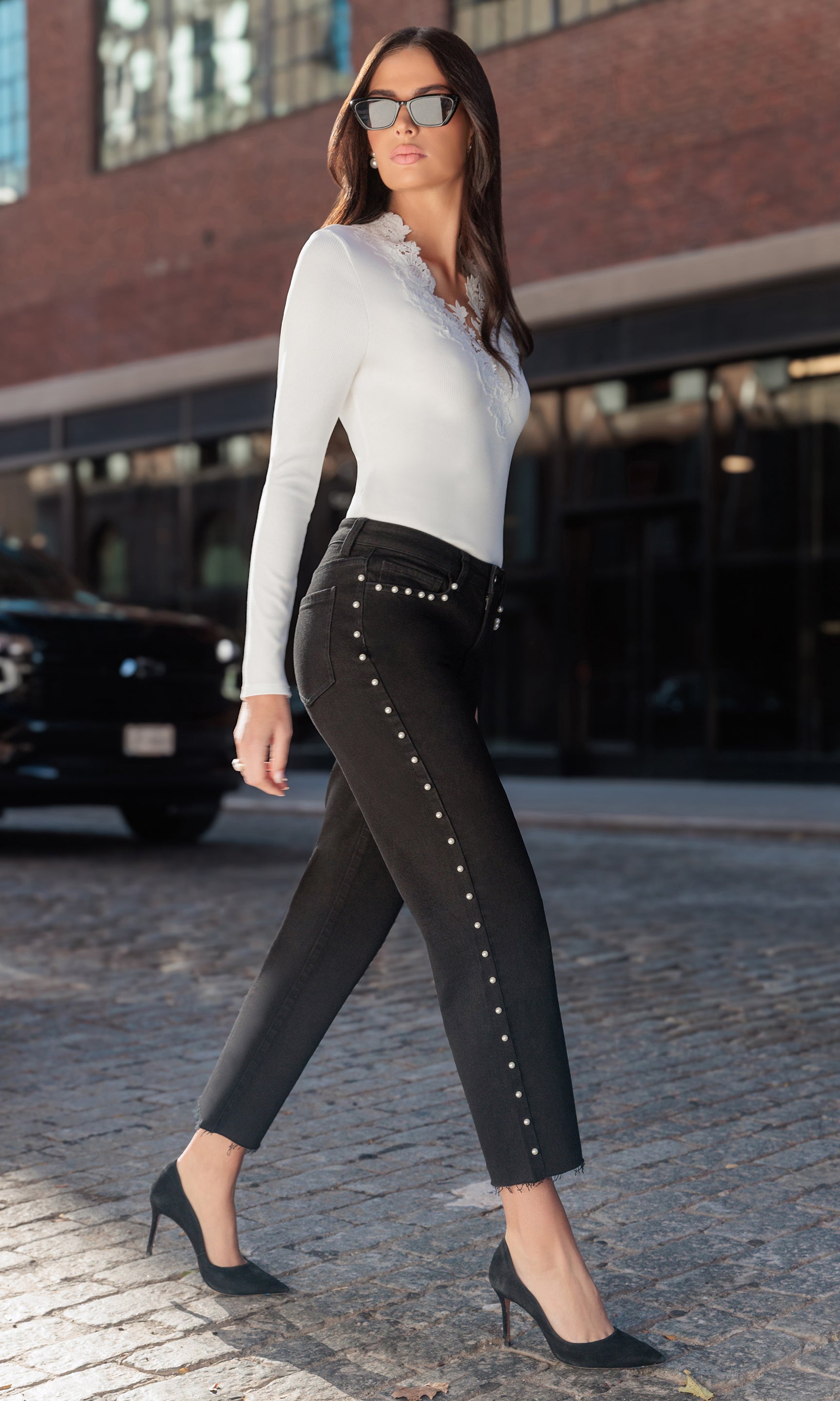 Woman wearing black pants with pearl details and a white top on a city street.