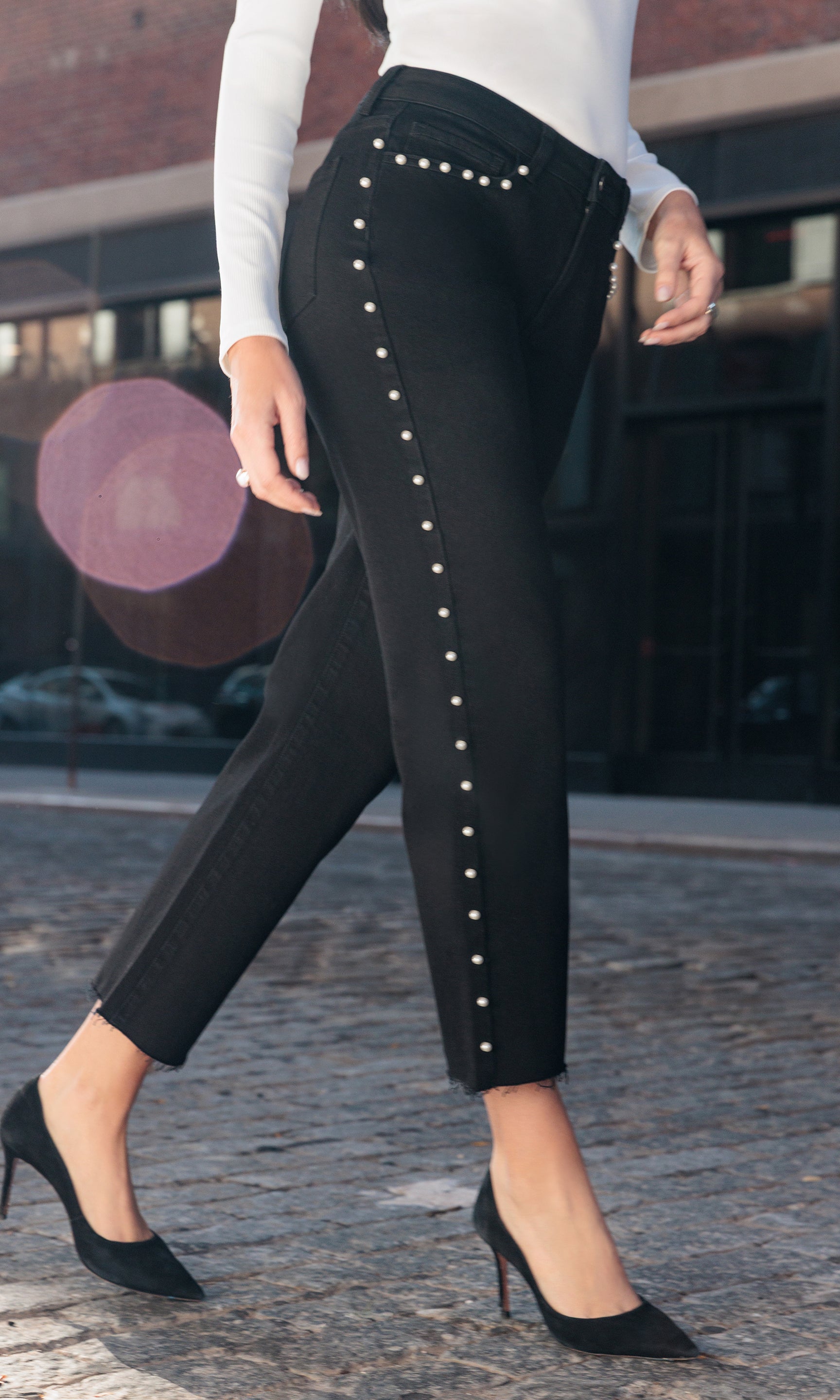 Black pants with white pearls worn by a person on a blurred street background