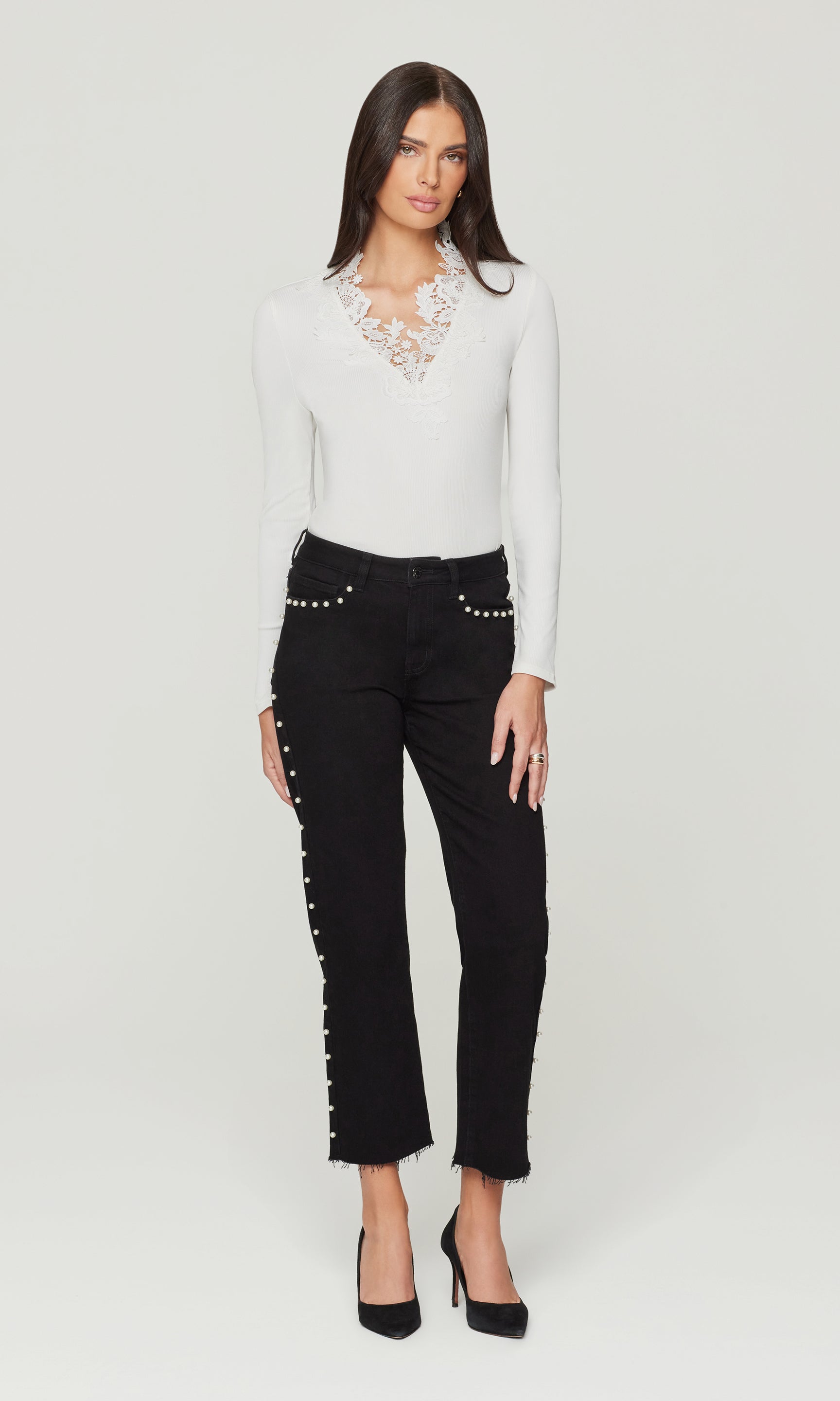 Woman wearing a white blouse with lace details and black pants with embellishments on a white background