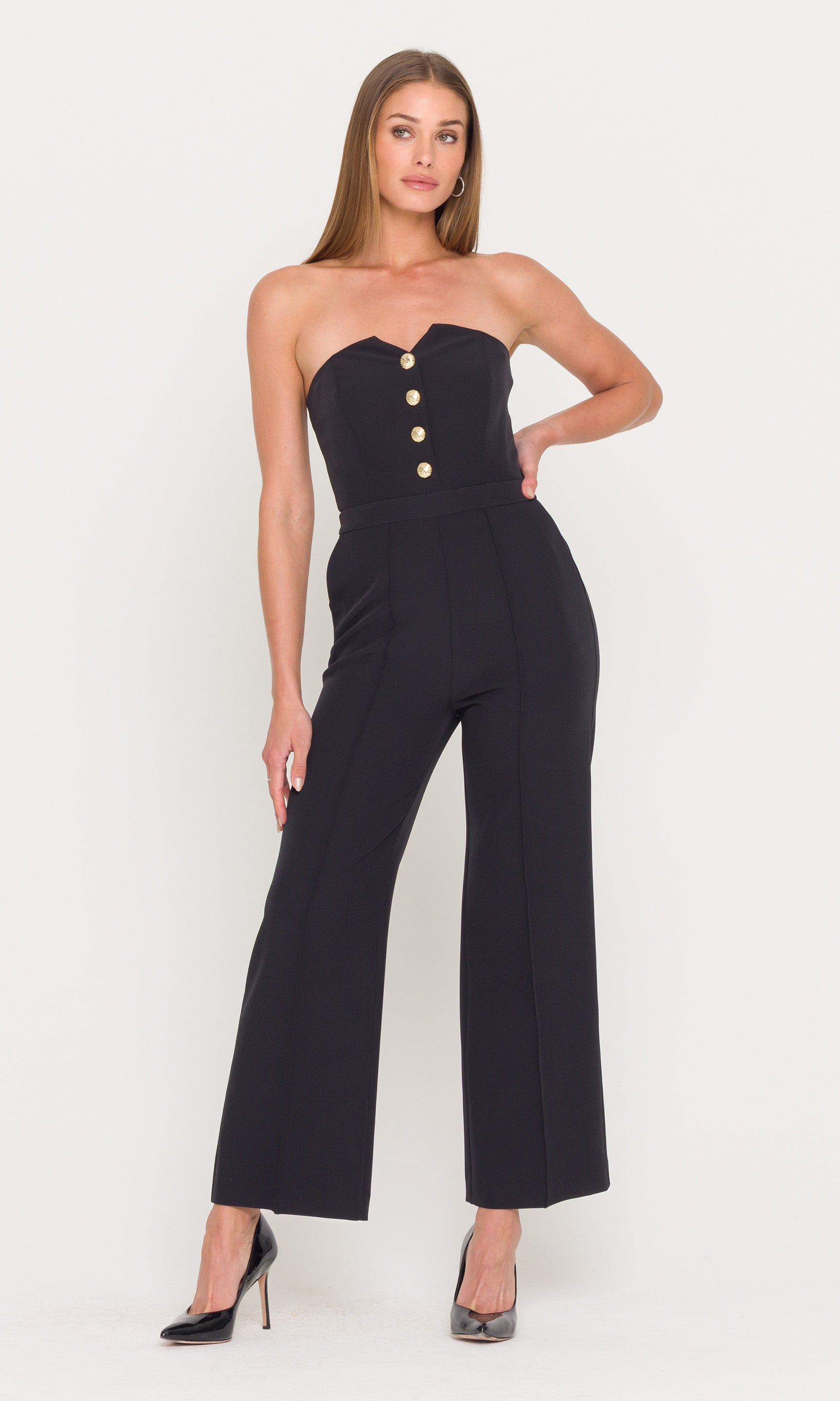 Woman wearing a black strapless jumpsuit with gold buttons on a white background