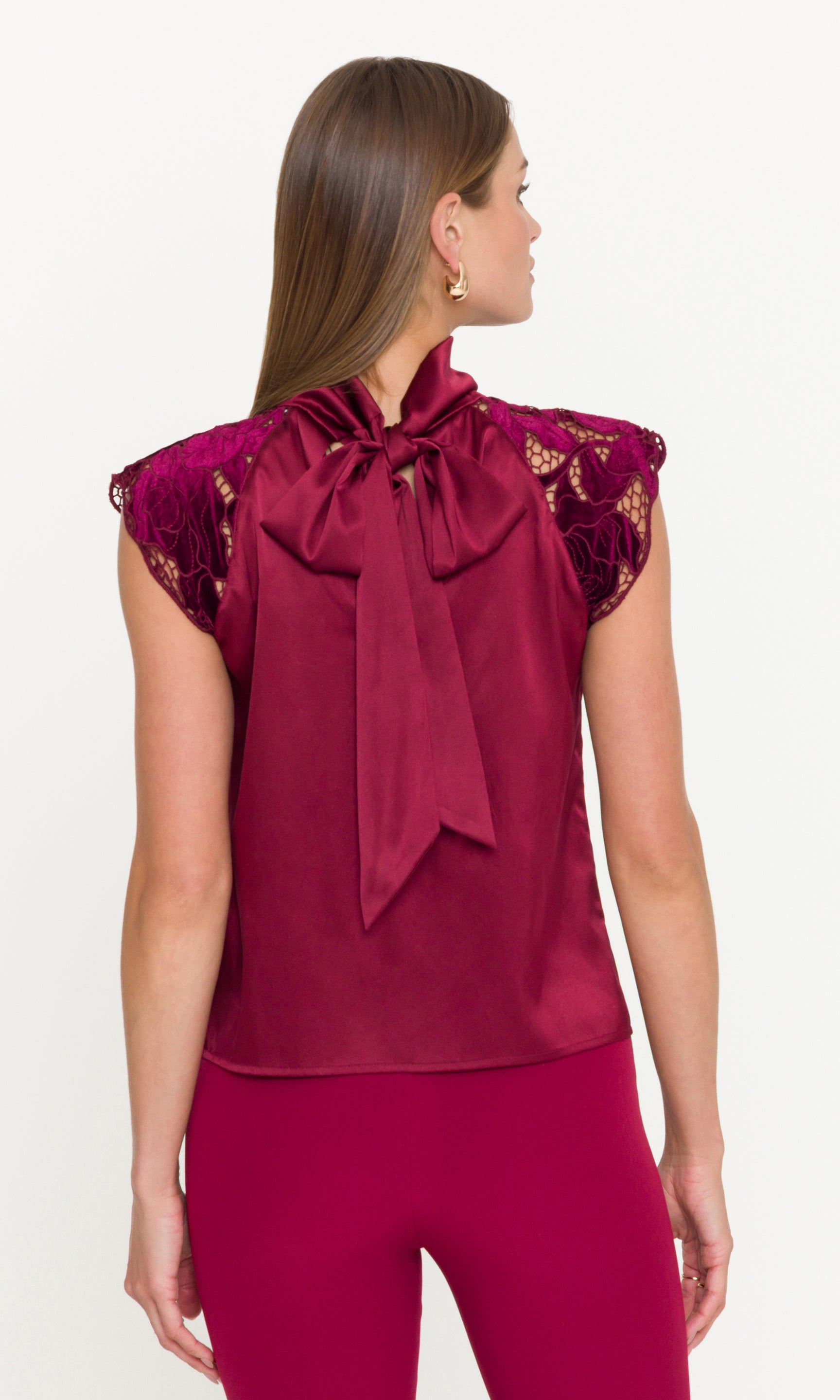 Woman wearing a burgundy top with lace details and a large bow on a white background