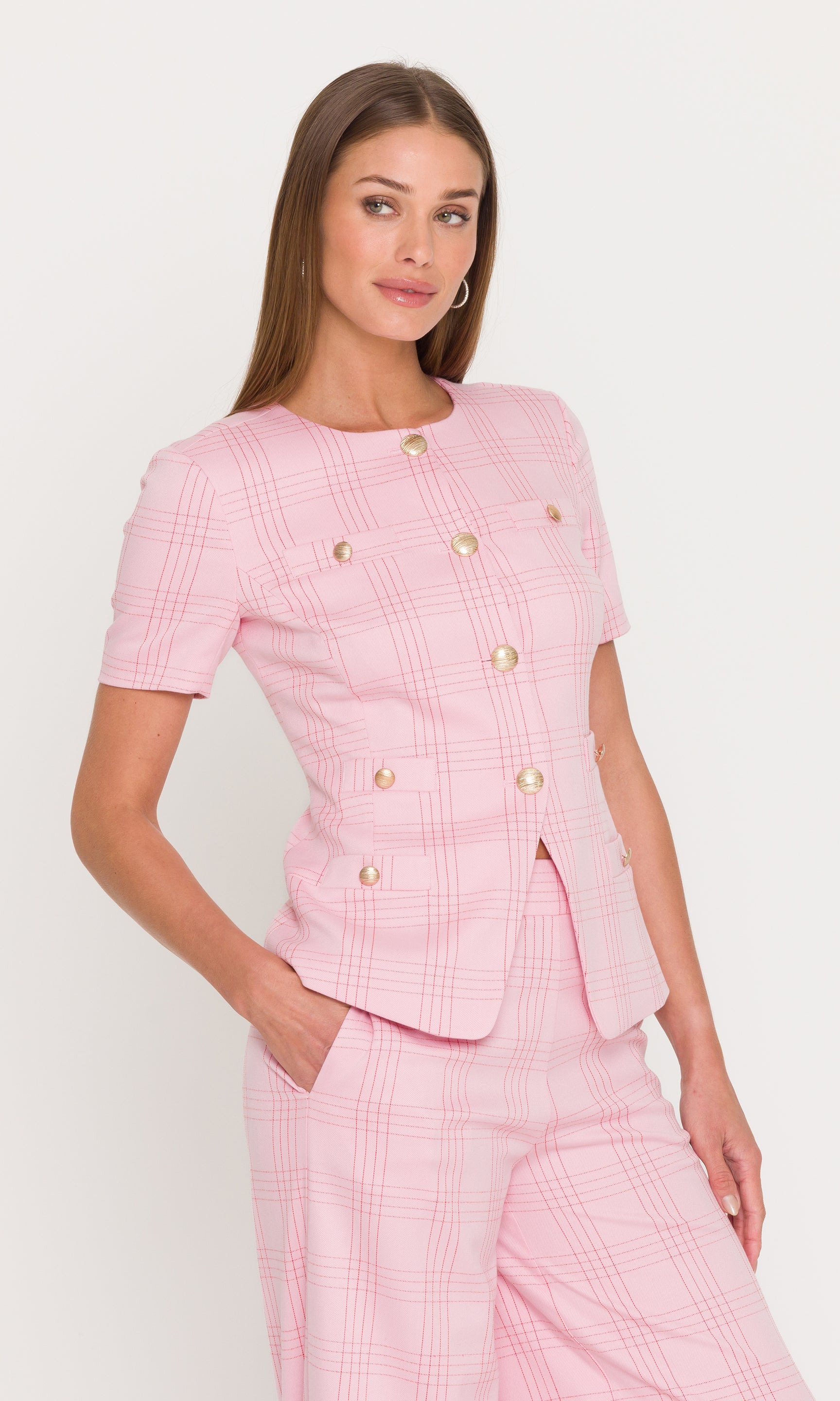 Side view of woman wearing a pink checkered outfit with a jacket and pants on a white background