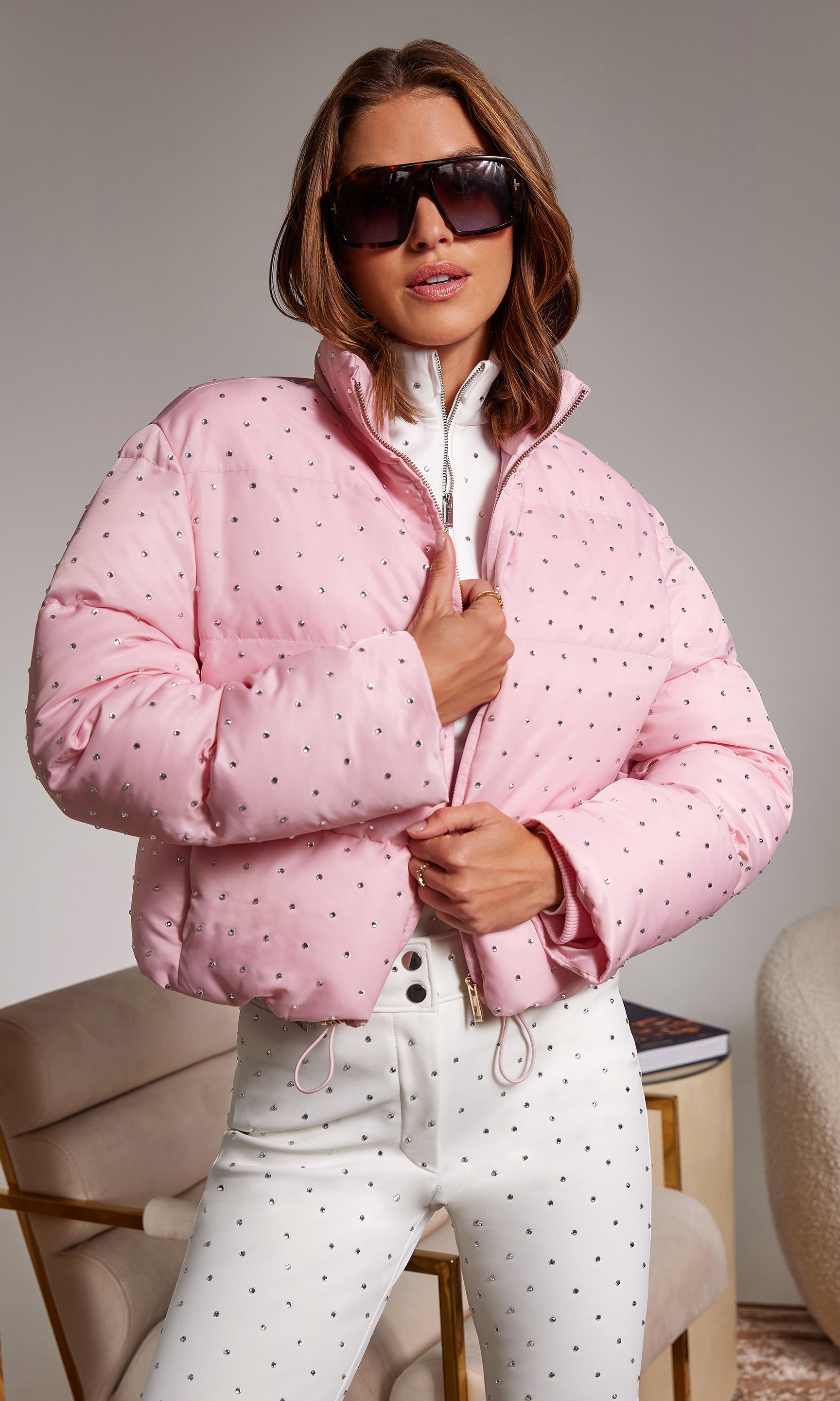 Woman wearing a pink puffer jacket with white crystals and matching pants indoors.