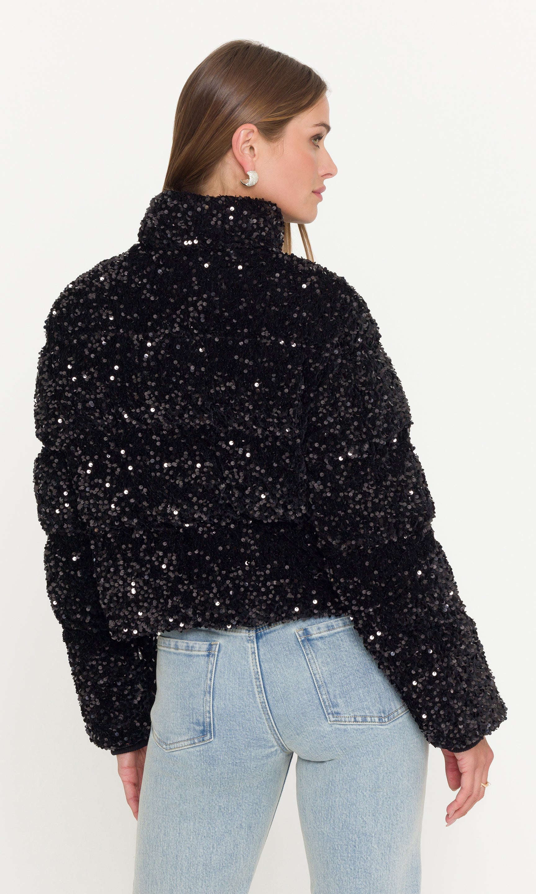Back view of model wearing a black sequin jacket and light blue jeans on a white background