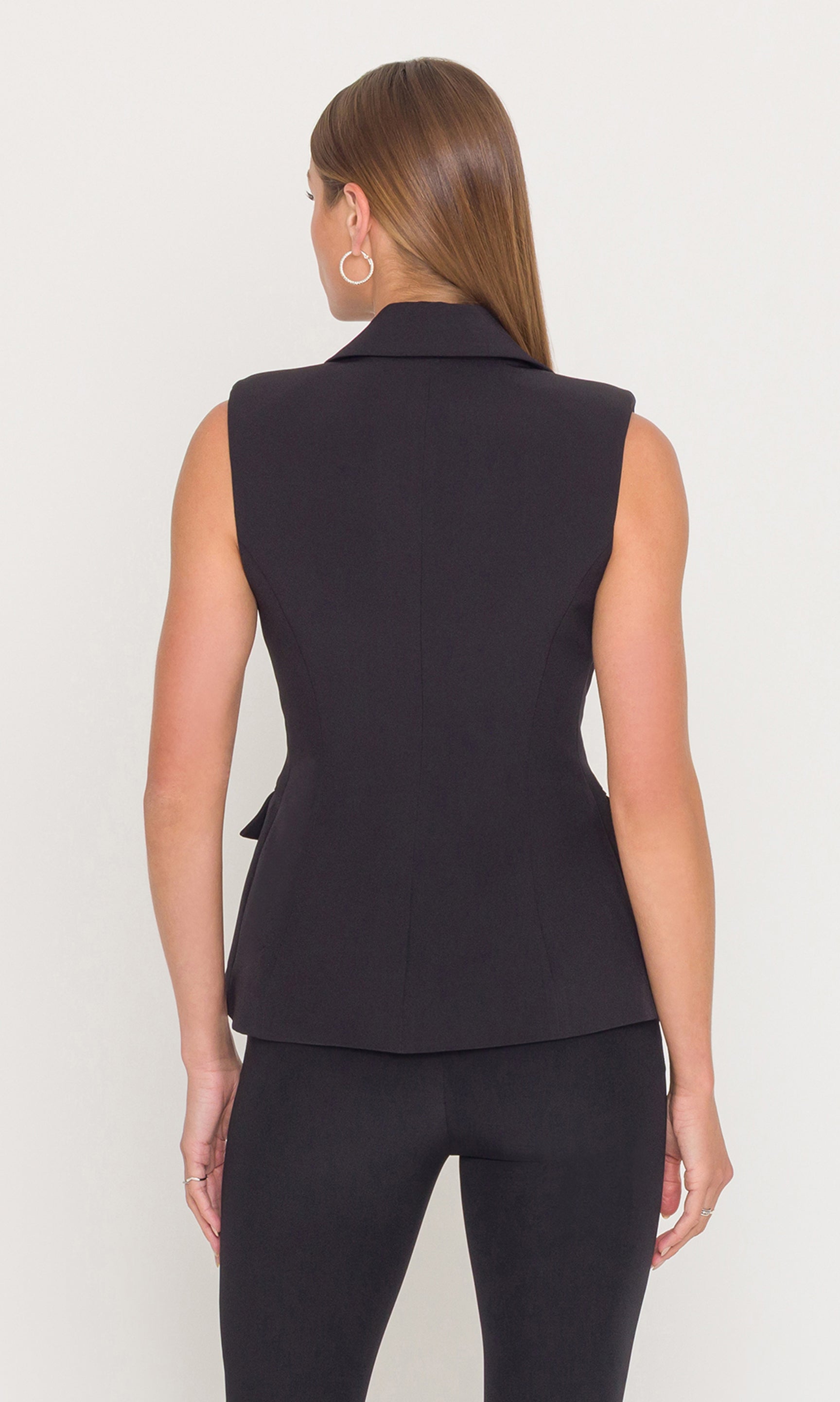 Back view of woman wearing a black sleeveless blazer on a white background