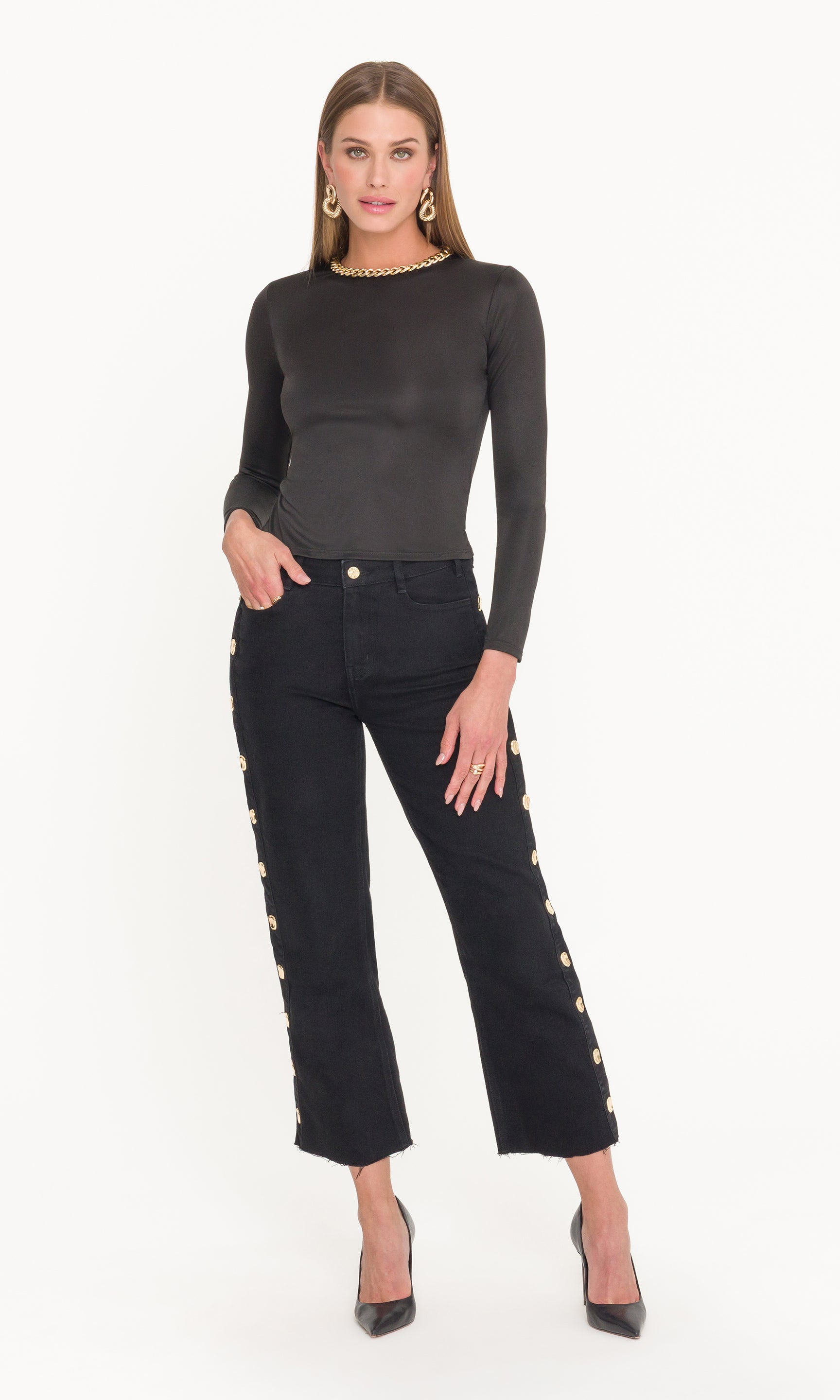 Full body image of model wearing a black long-sleeve top and black jeans with gold buttons on a white background
