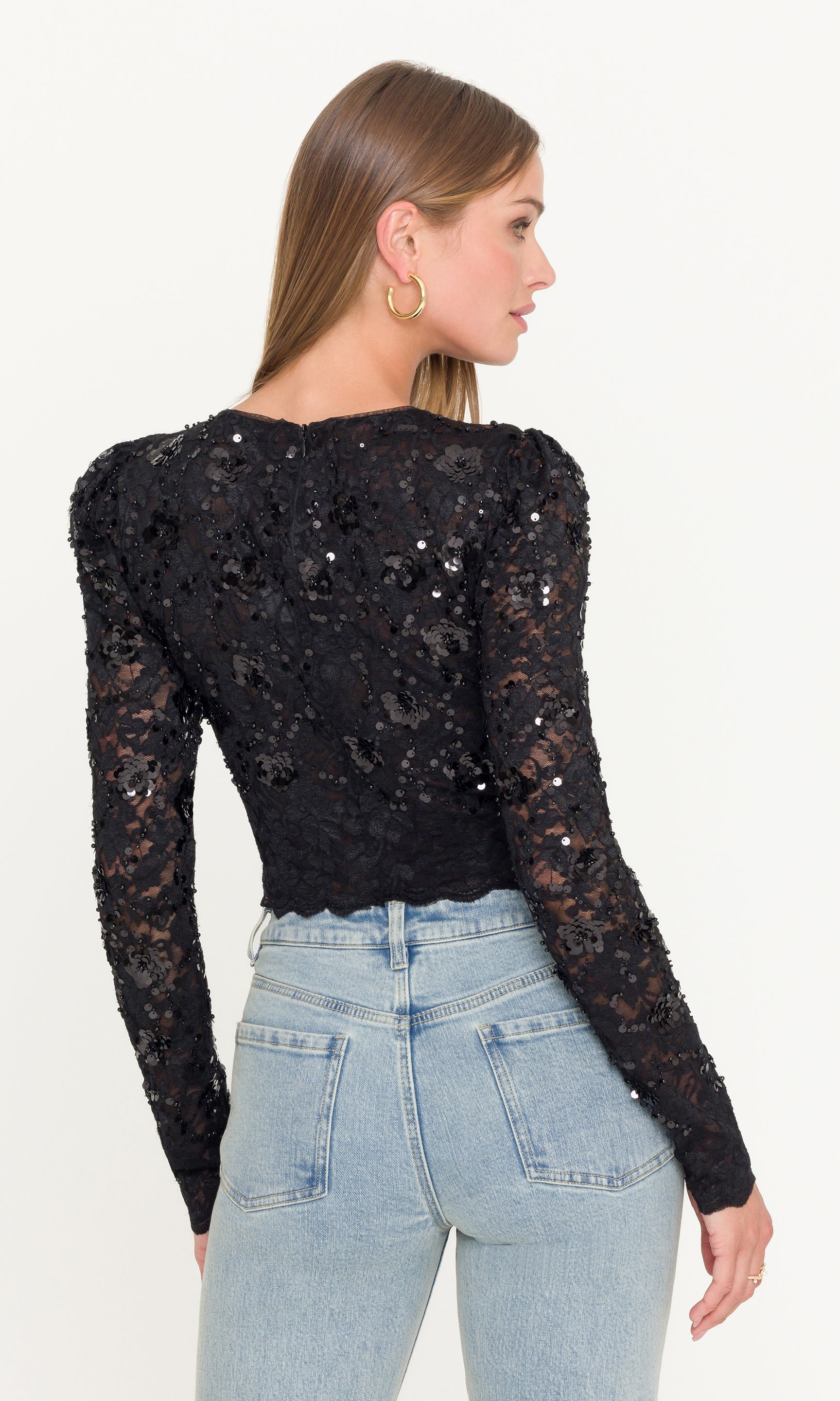 Back view of model wearing a black sequin long-sleeve top and light blue jeans on a white background