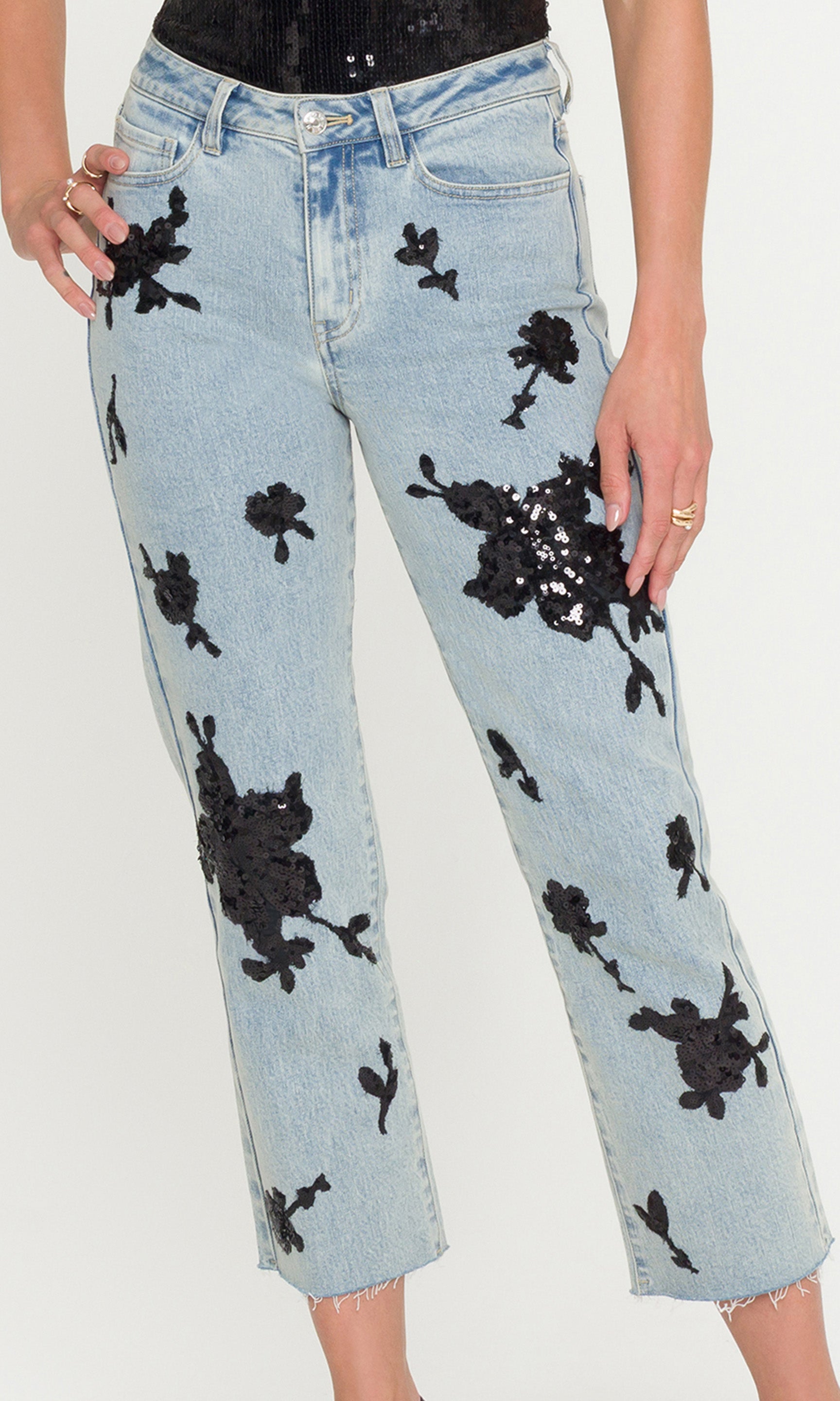 Close-up of light blue jeans with black floral sequin patterns worn by a person on a white background
