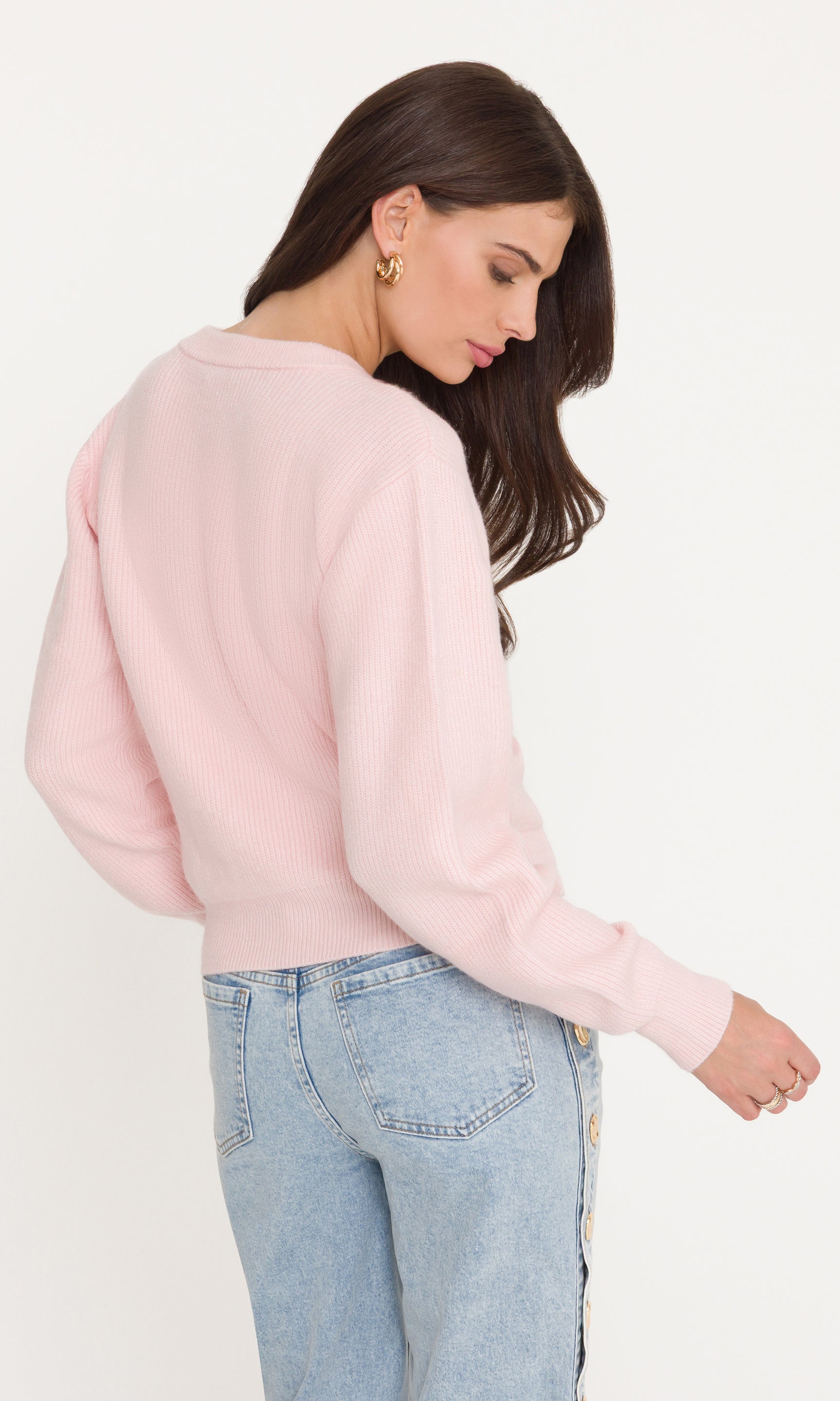 Woman wearing a light pink sweater and light blue jeans on a white background