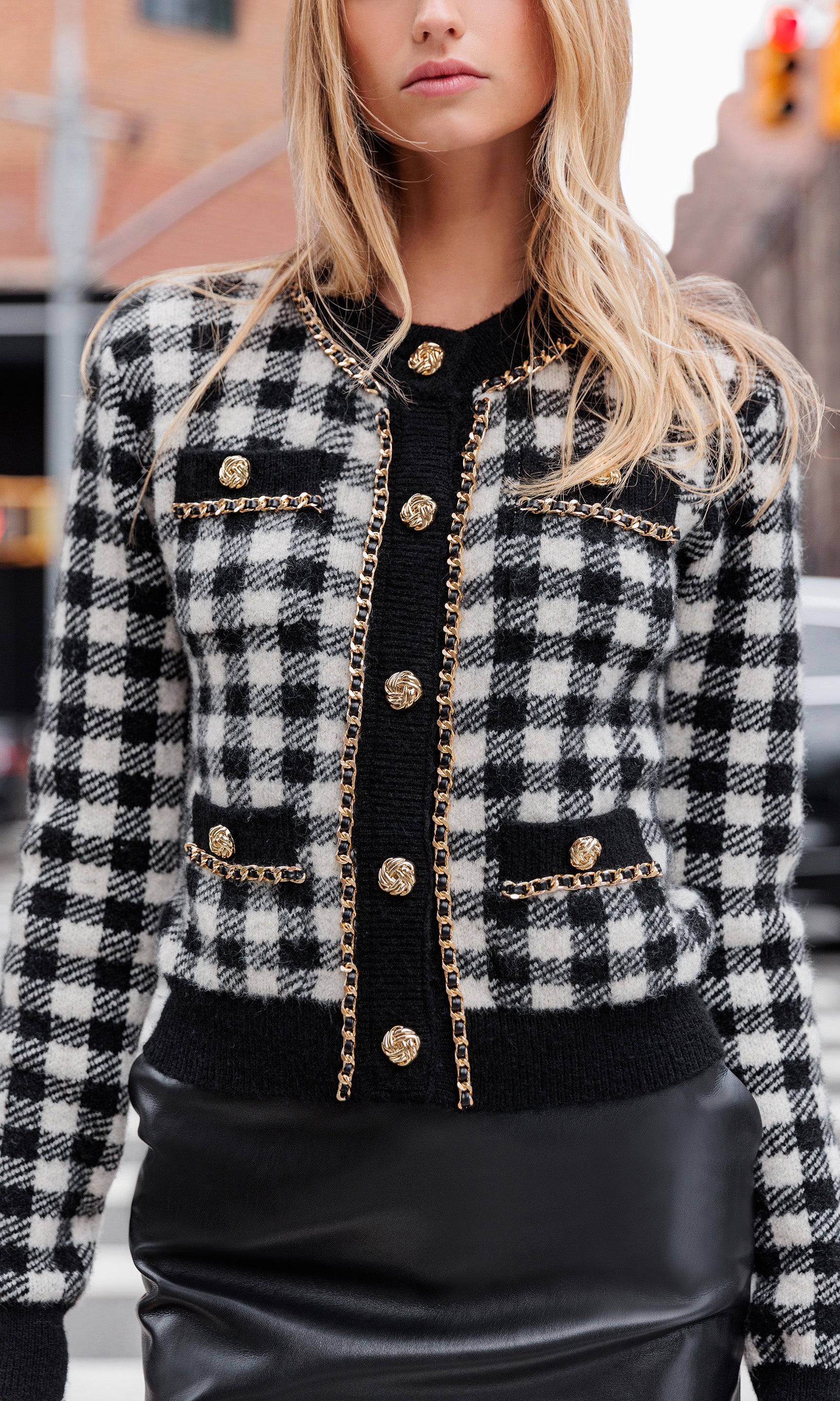 Person wearing a black and white checkered cardigan with gold buttons in an urban setting